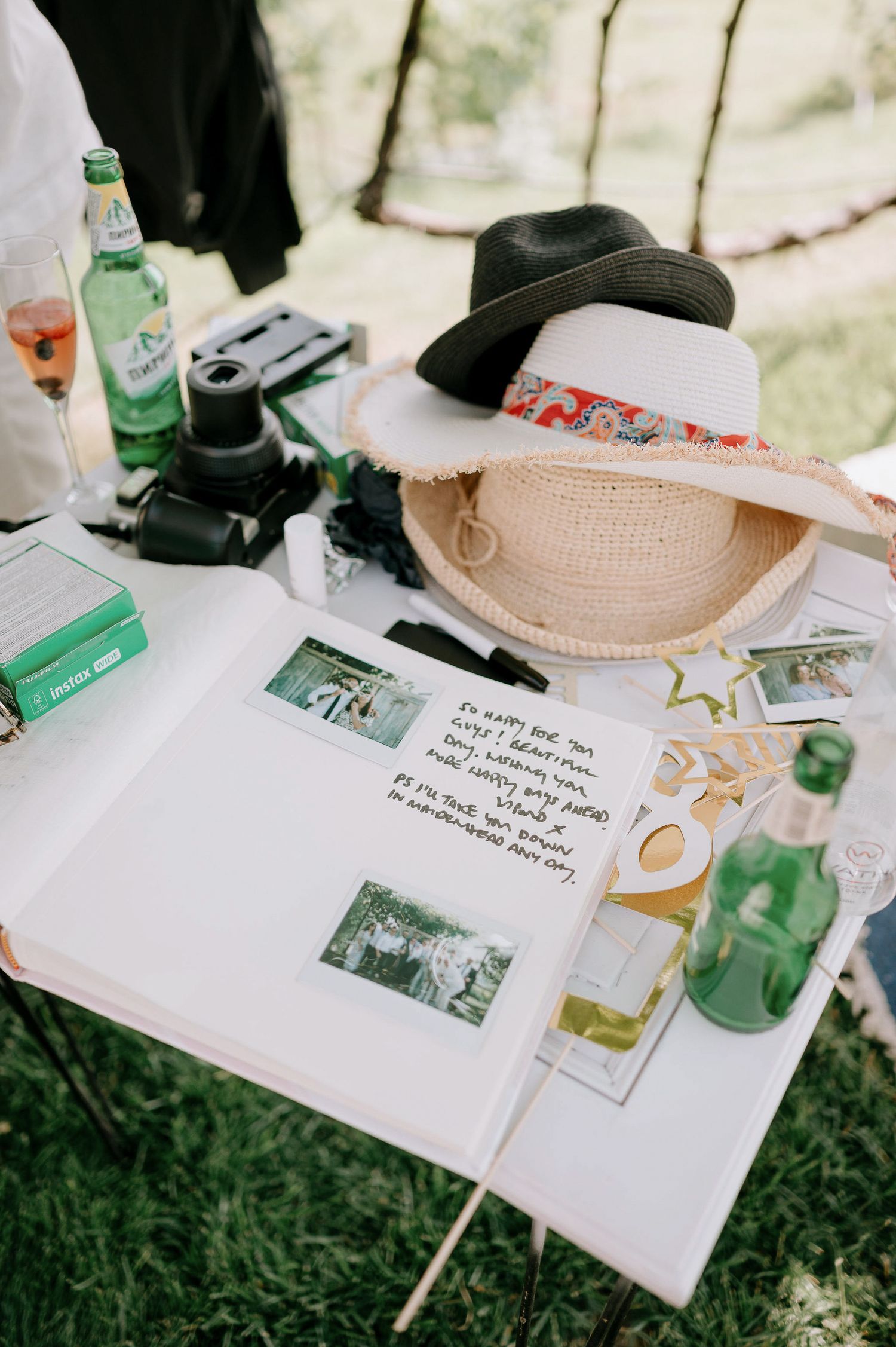 A wedding guestbook display featuring hats, cameras, and polaroid photos on a white table.