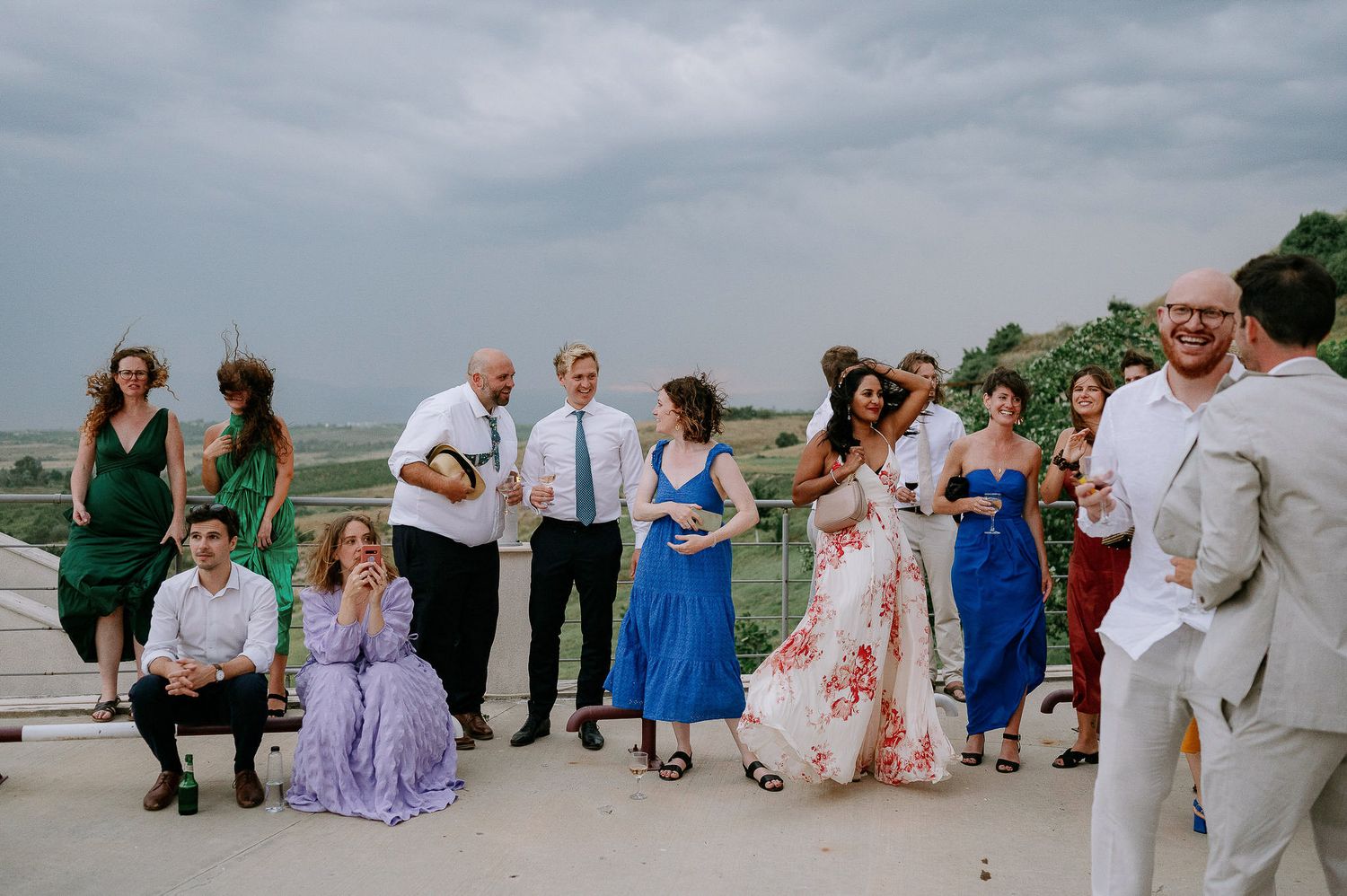 Wedding party and guests gather on a terrace during an outdoor celebration.