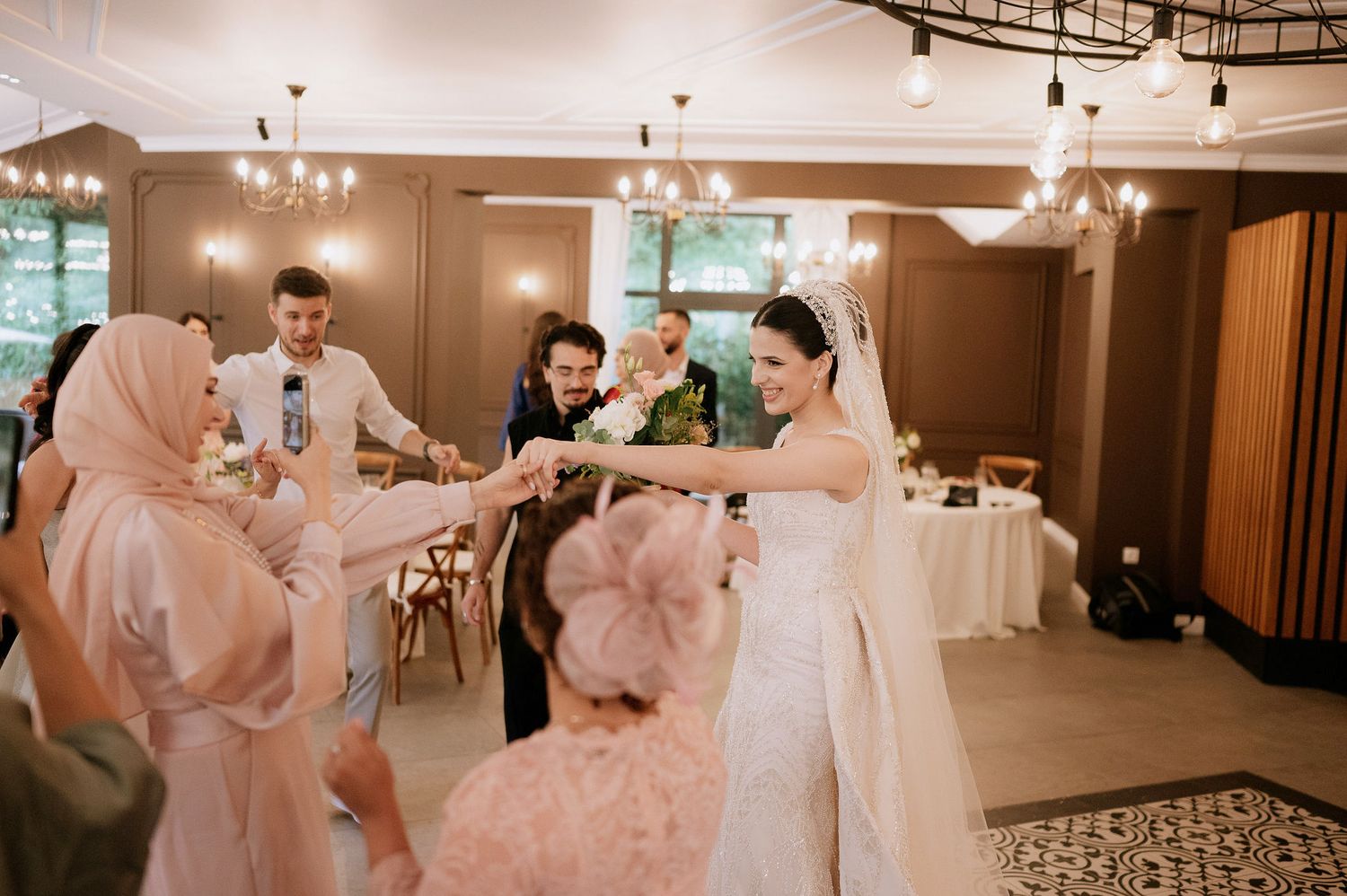 Wedding celebration in modern reception hall with chandelier lighting and decorative details.