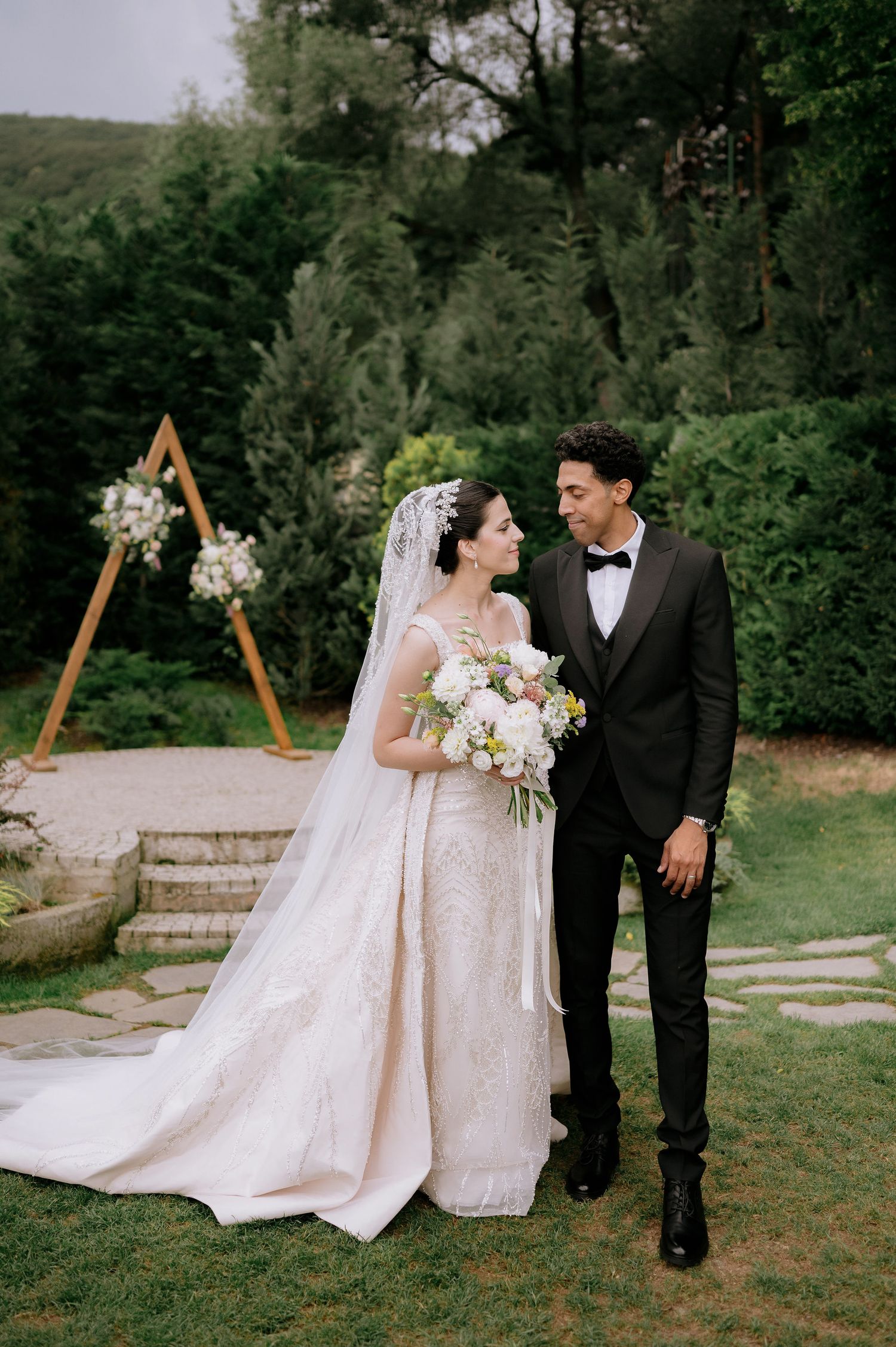 Wedding couple posing in front of a wooden triangle arch in a garden setting.