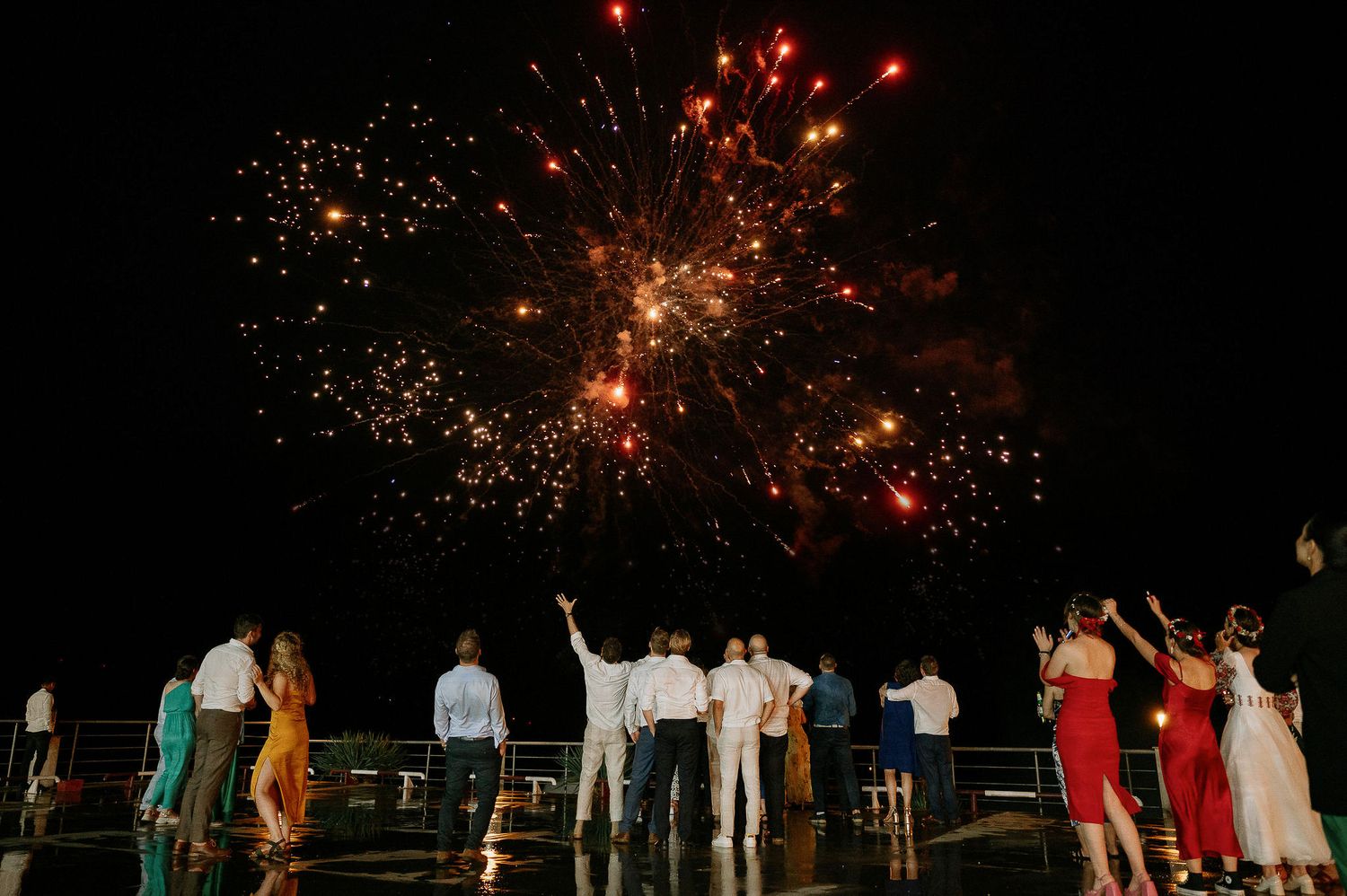 Colorful fireworks burst overhead as wedding attendees gather to watch the display.