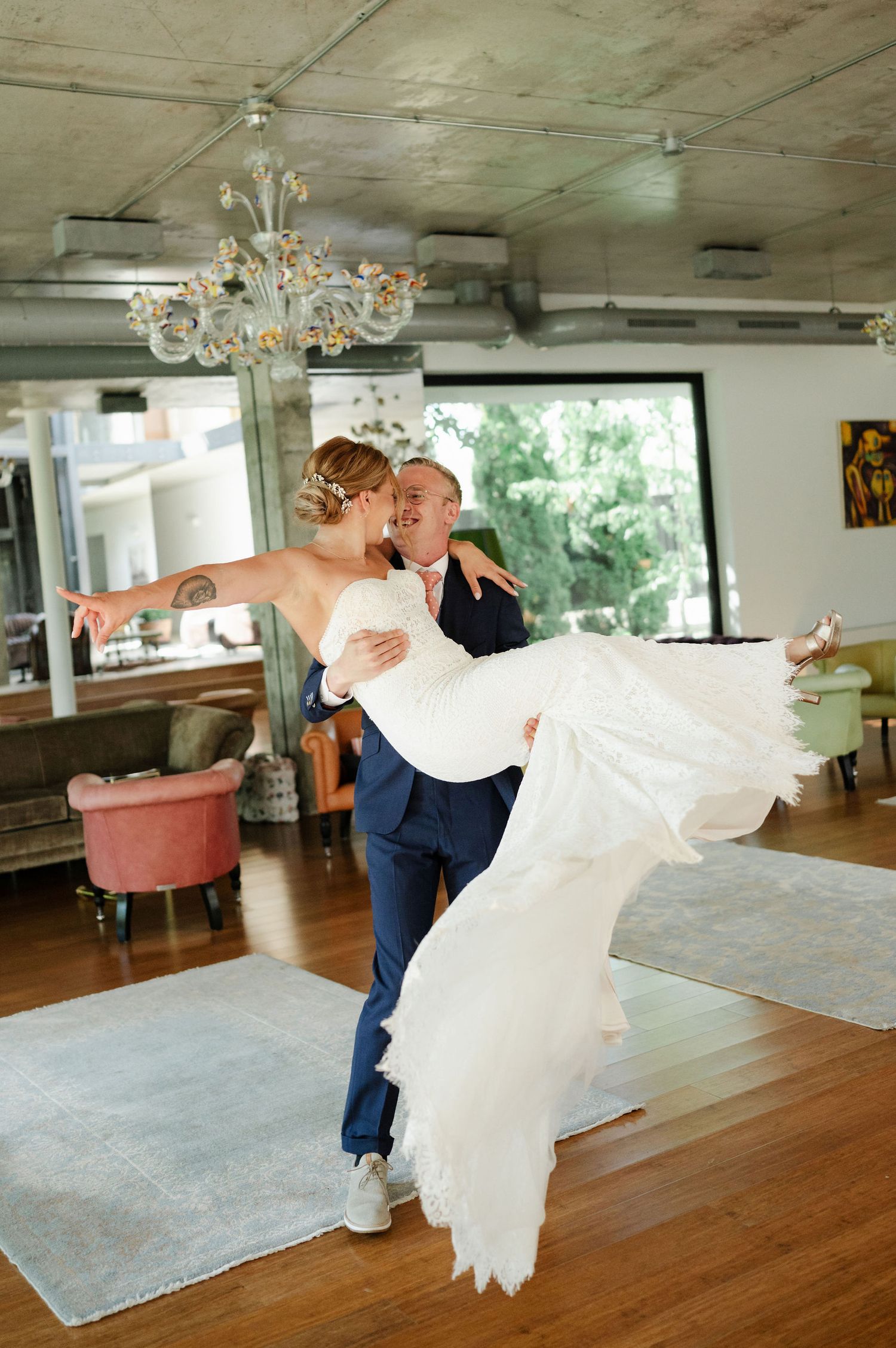 A romantic first dance moment in an elegant venue with hardwood floors and chandeliers overhead.