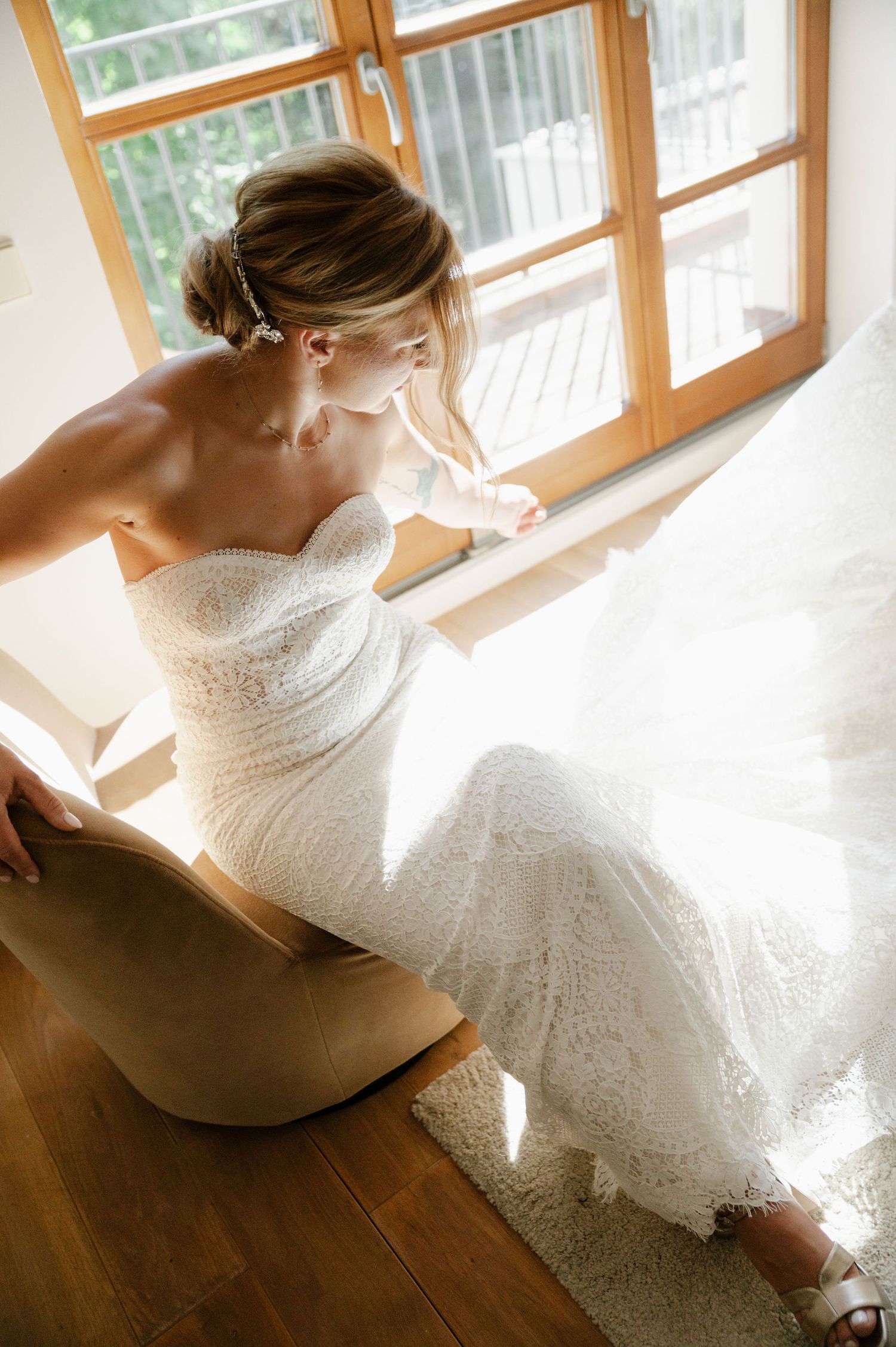 Soft natural light illuminates a wedding dress through wooden windows in an intimate indoor setting.