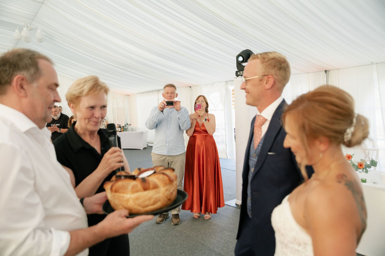 Wedding celebration under white tent with traditional bread presentation ceremony.