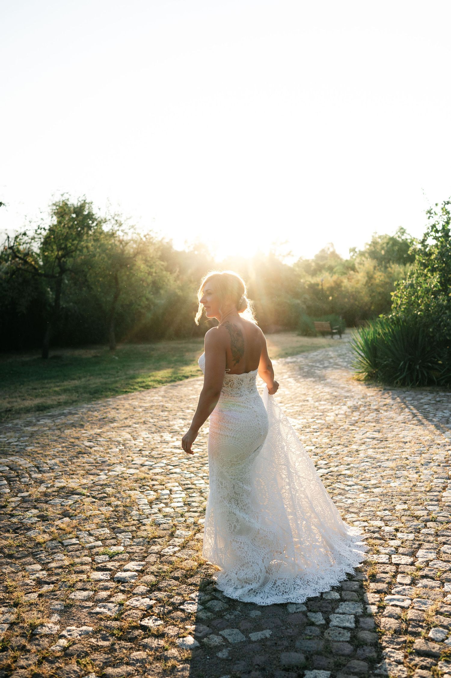 Elegant bridal portrait on cobblestone path with dramatic backlighting.