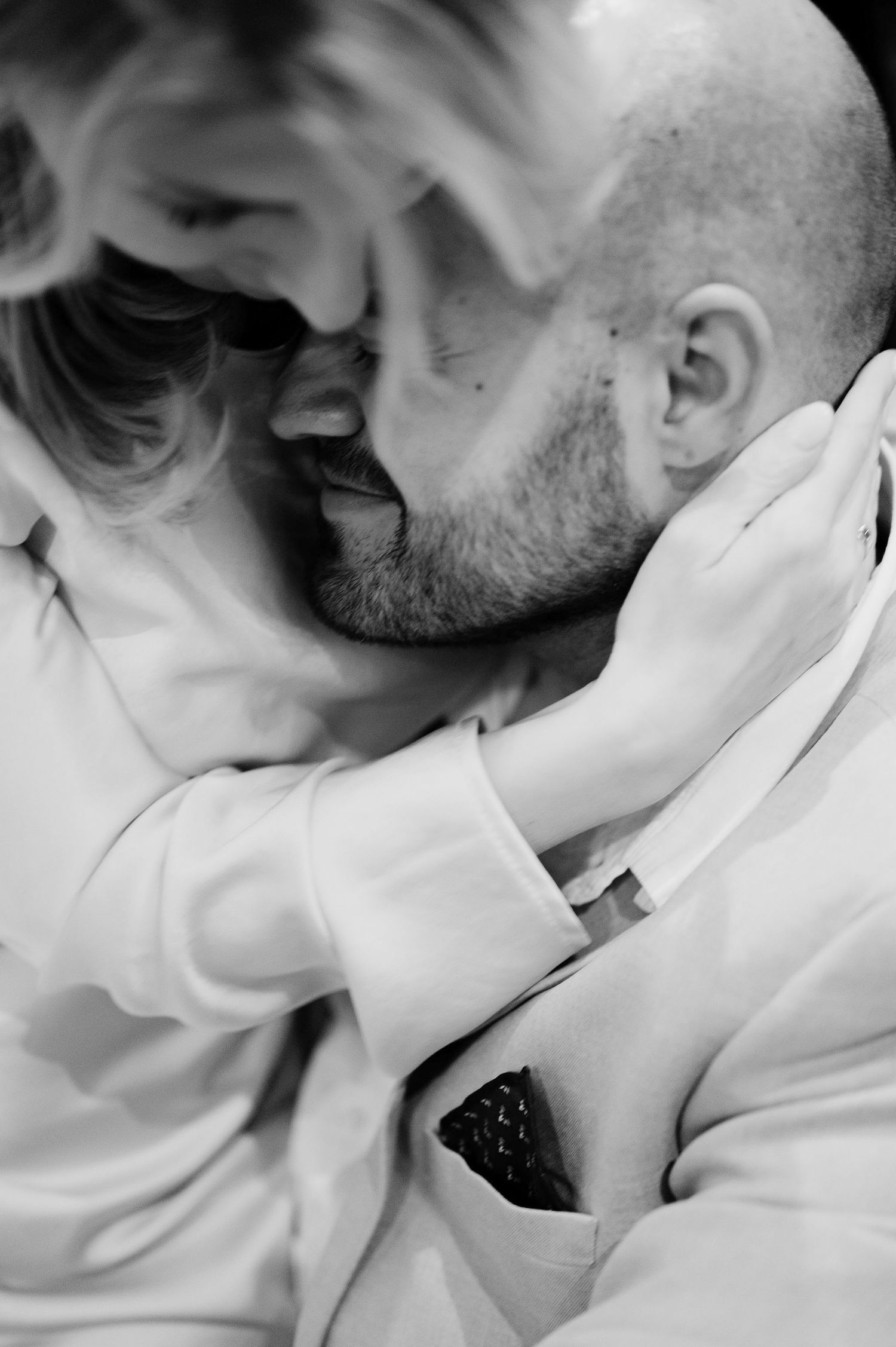 Black and white close-up shots of a tender embrace between two people in white clothing.