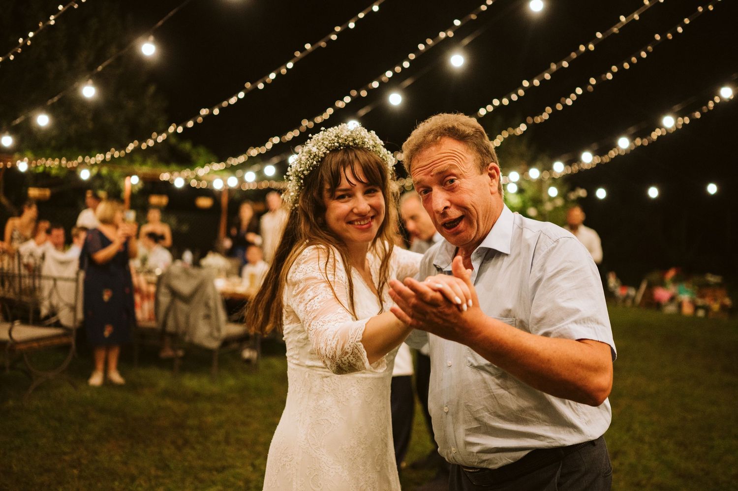 Couples dancing under romantic string lights at an outdoor wedding reception.