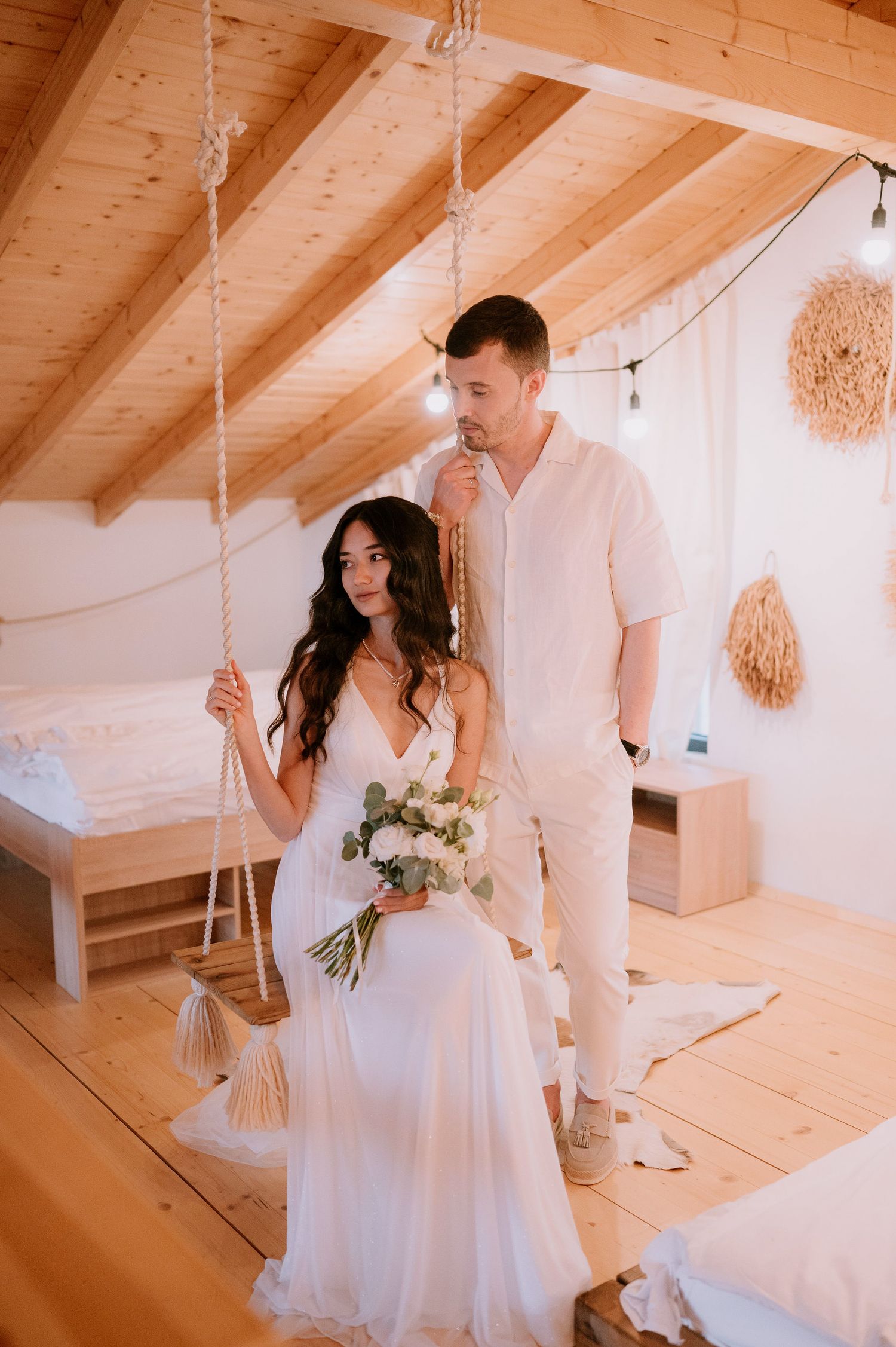 Wedding photography session in a light-filled room with wooden beams and hanging decorations.