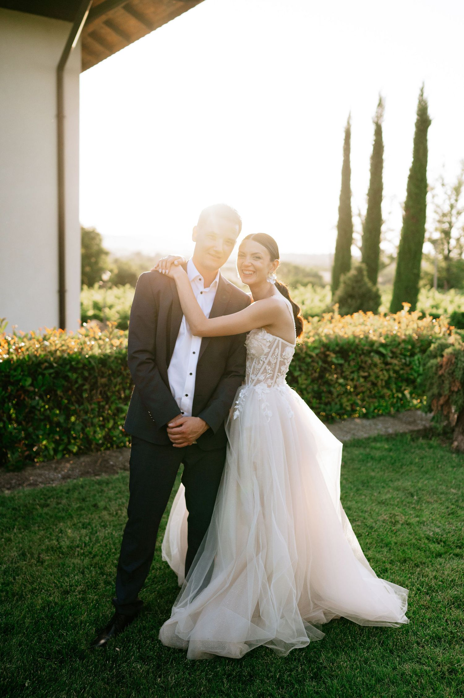 Newlyweds share an intimate moment dancing outdoors at golden hour with cypress trees in the background.