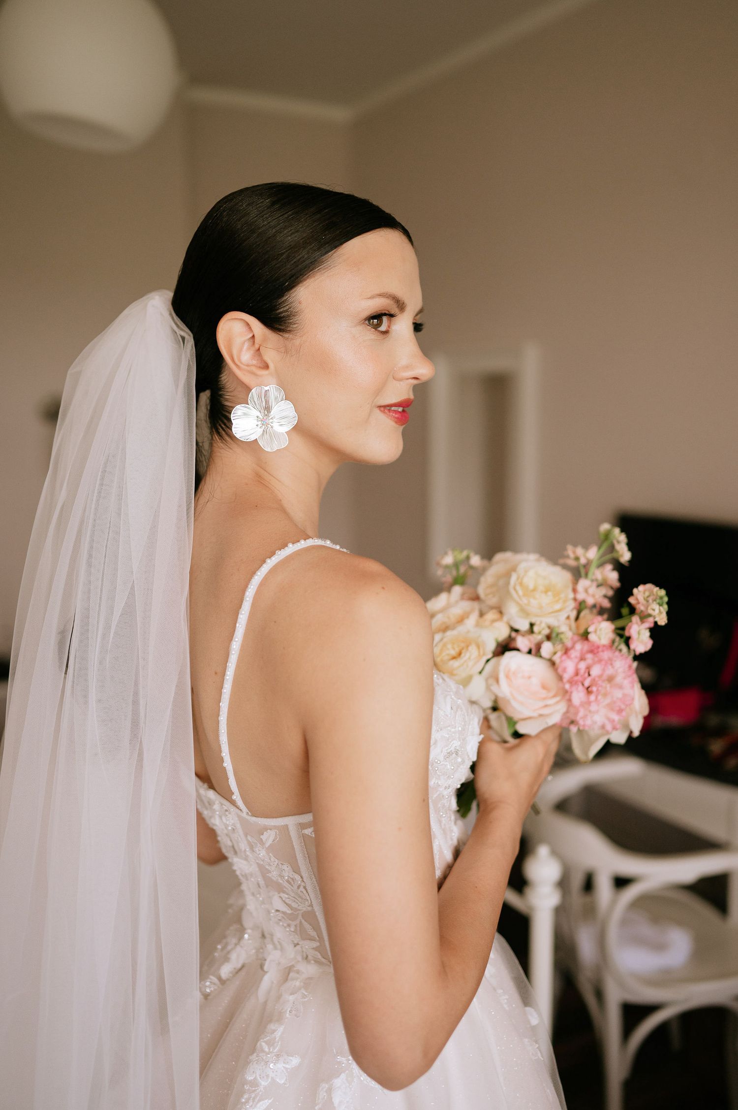 Side profile of bride holding a romantic bouquet in a sun-filled room.
