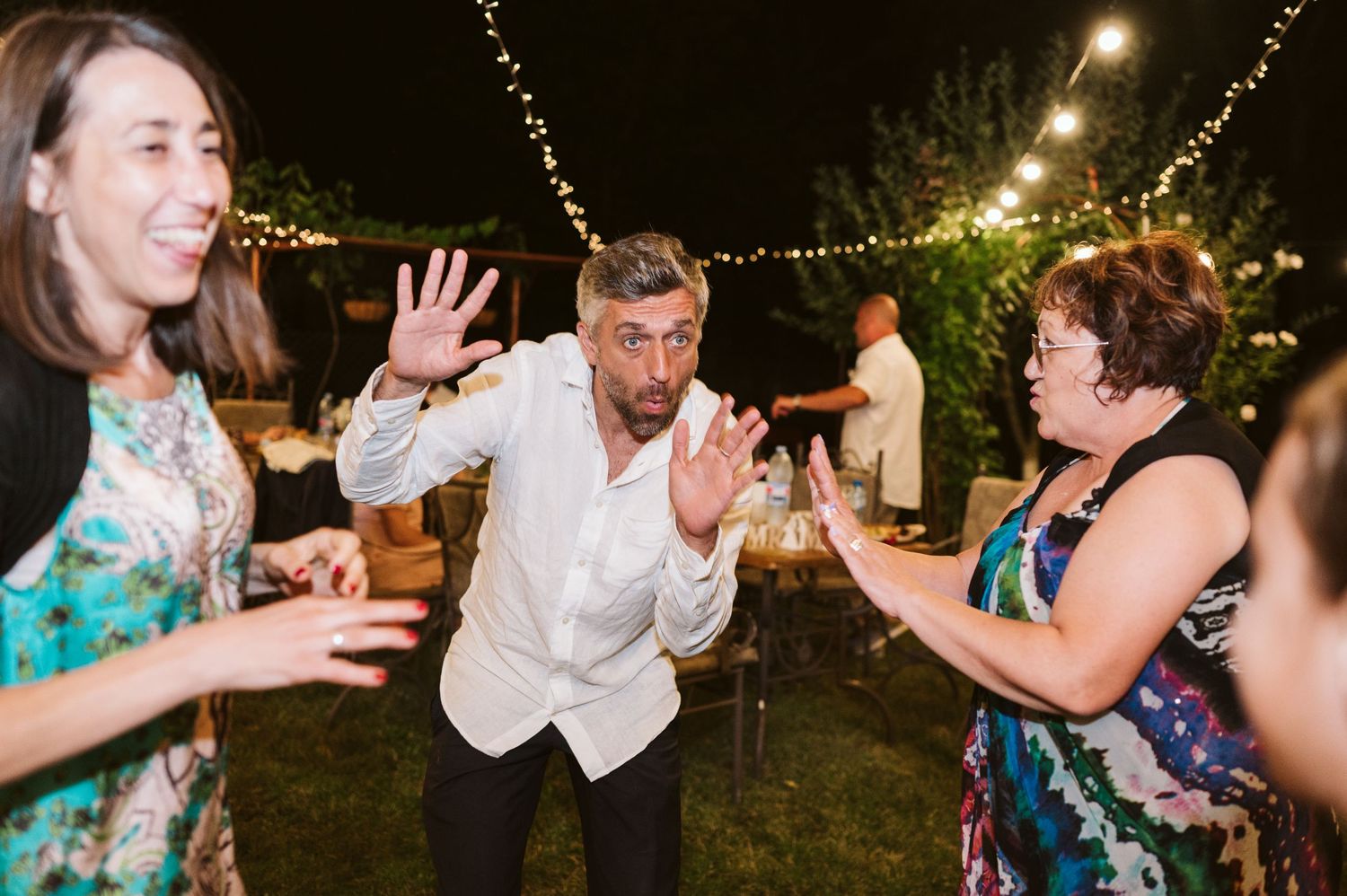 Wedding guests dance enthusiastically under string lights at an outdoor reception.