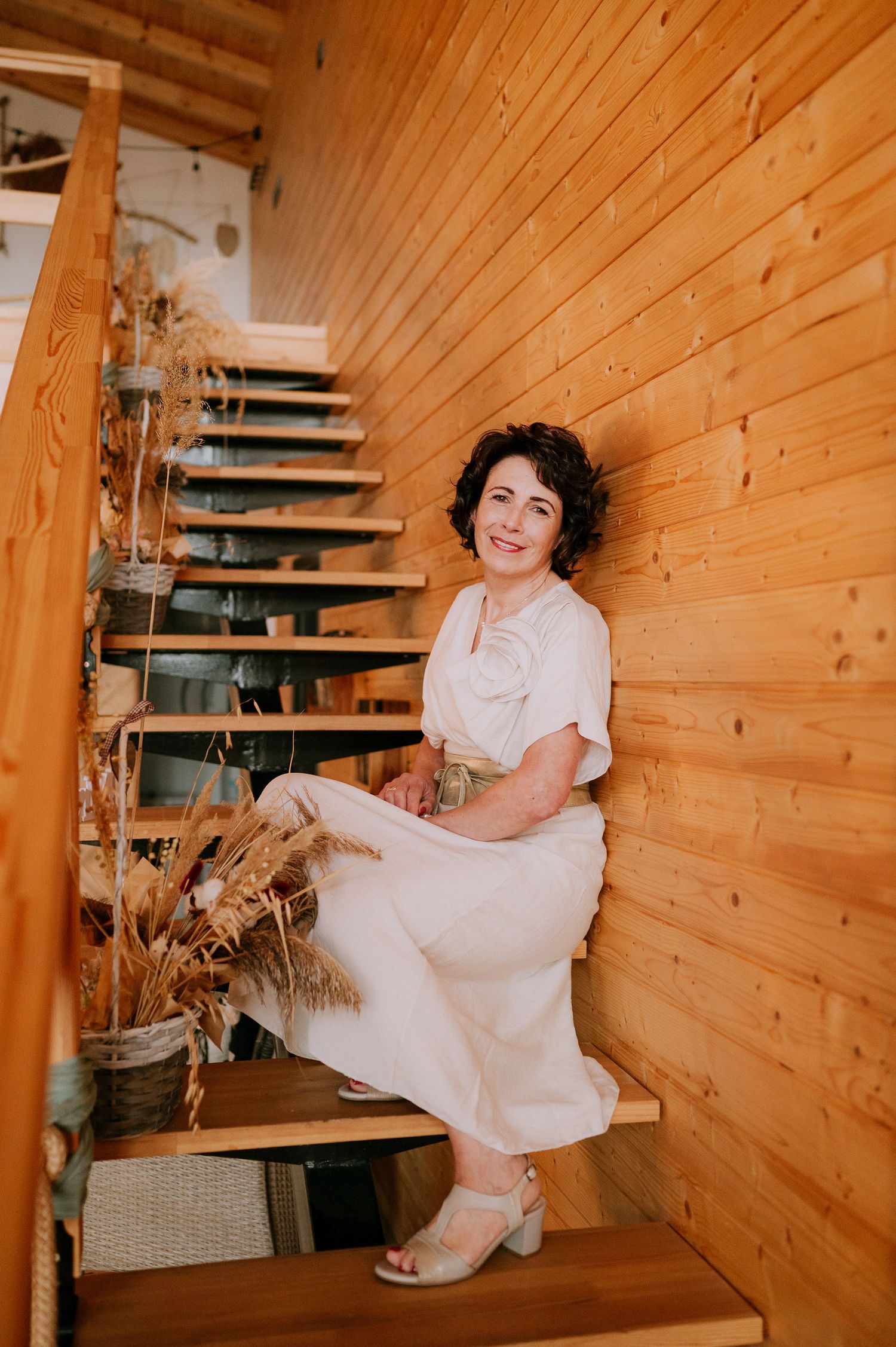 A person in white sits on wooden stairs in a rustic venue with natural wood paneling.