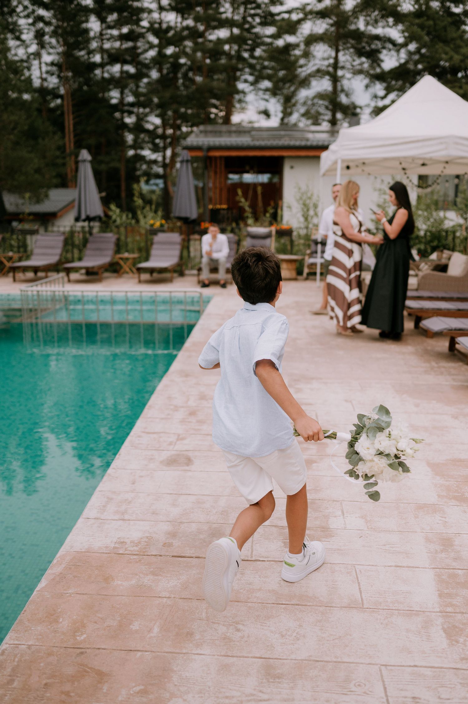 Wedding guests dance and celebrate on a stone patio next to a turquoise pool.