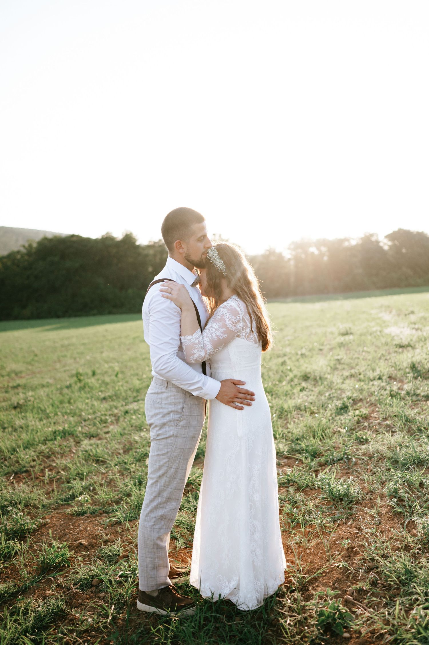 A romantic sunset wedding portrait of a couple embracing in a grassy field.