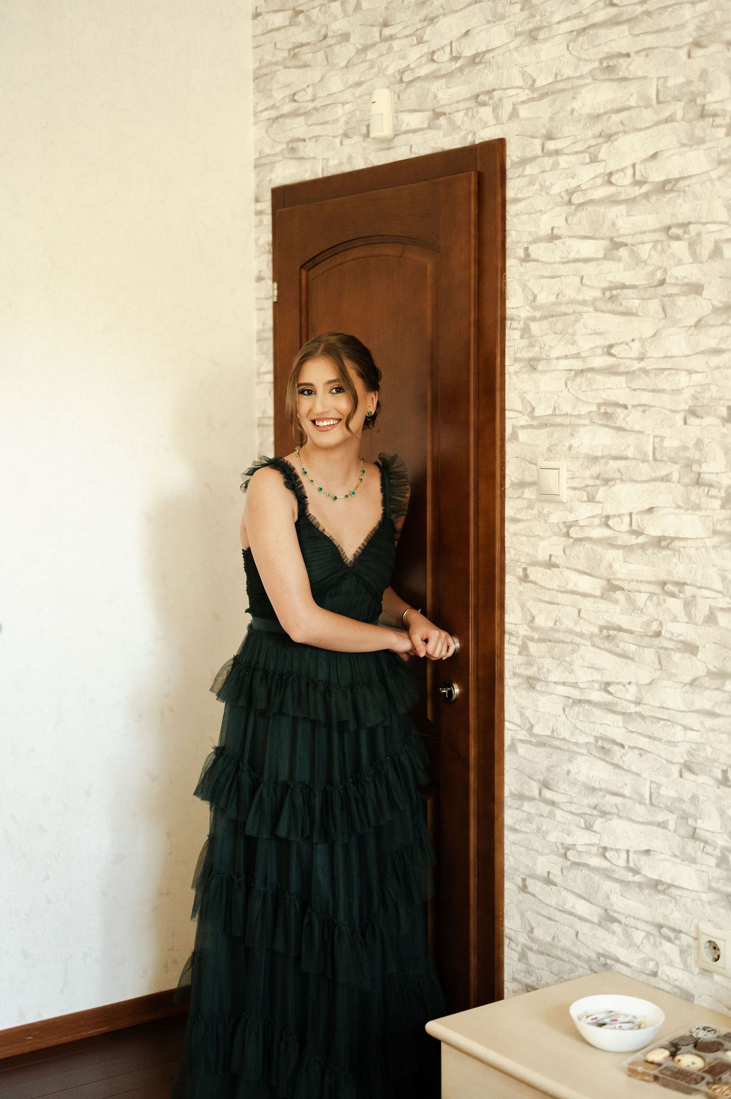 Person in a flowing black tiered dress twirling and posing against a textured white wall.