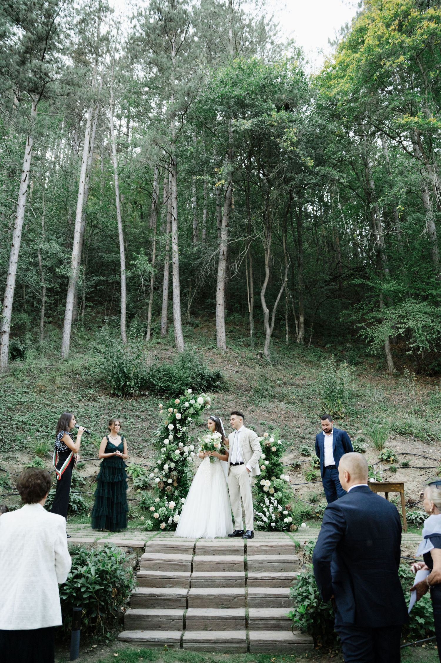 Wedding ceremony setup in woodland setting with tiered stone steps and white floral decor.