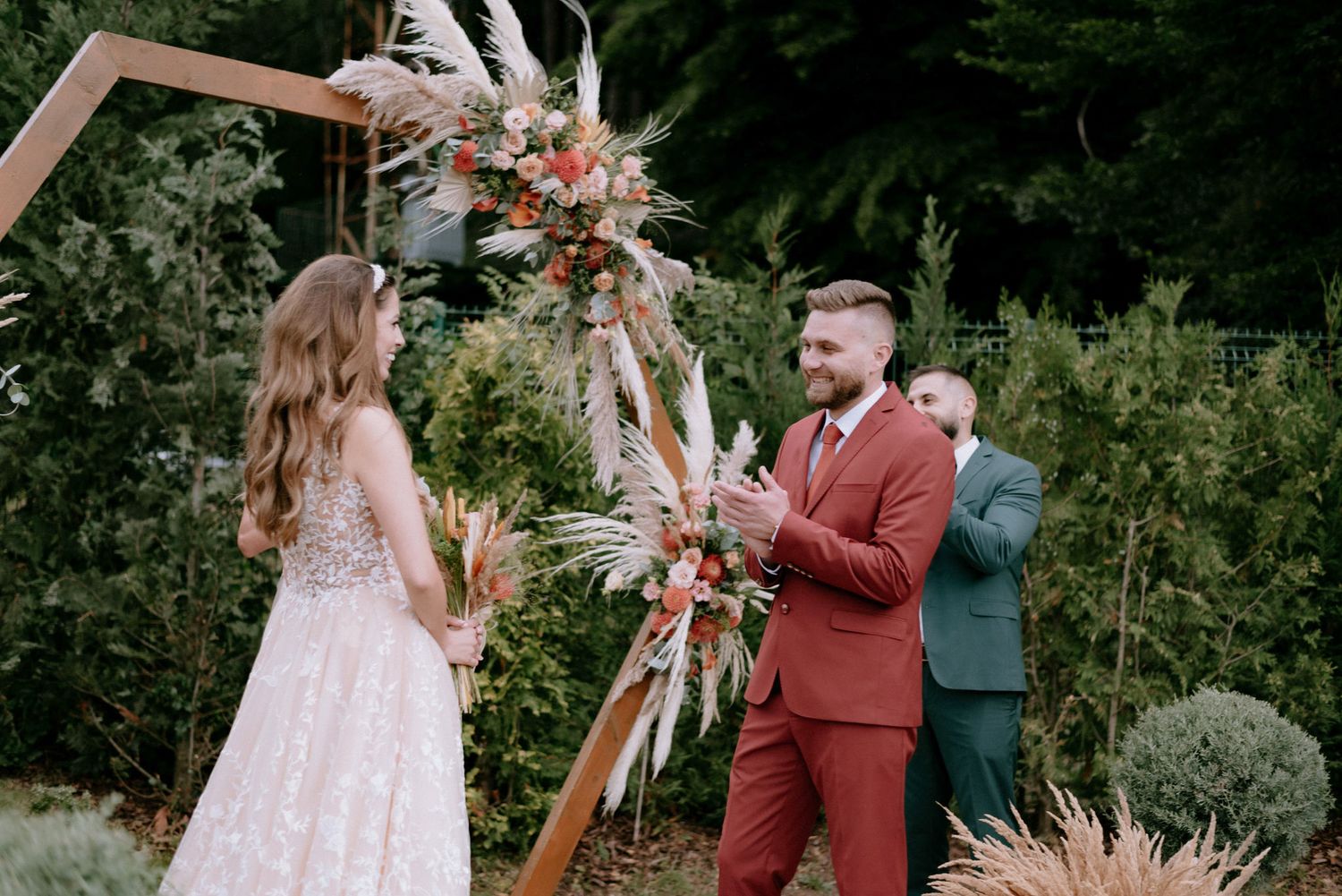 A couple shares a romantic moment during their outdoor wedding ceremony surrounded by lush greenery and floral arrangements.
