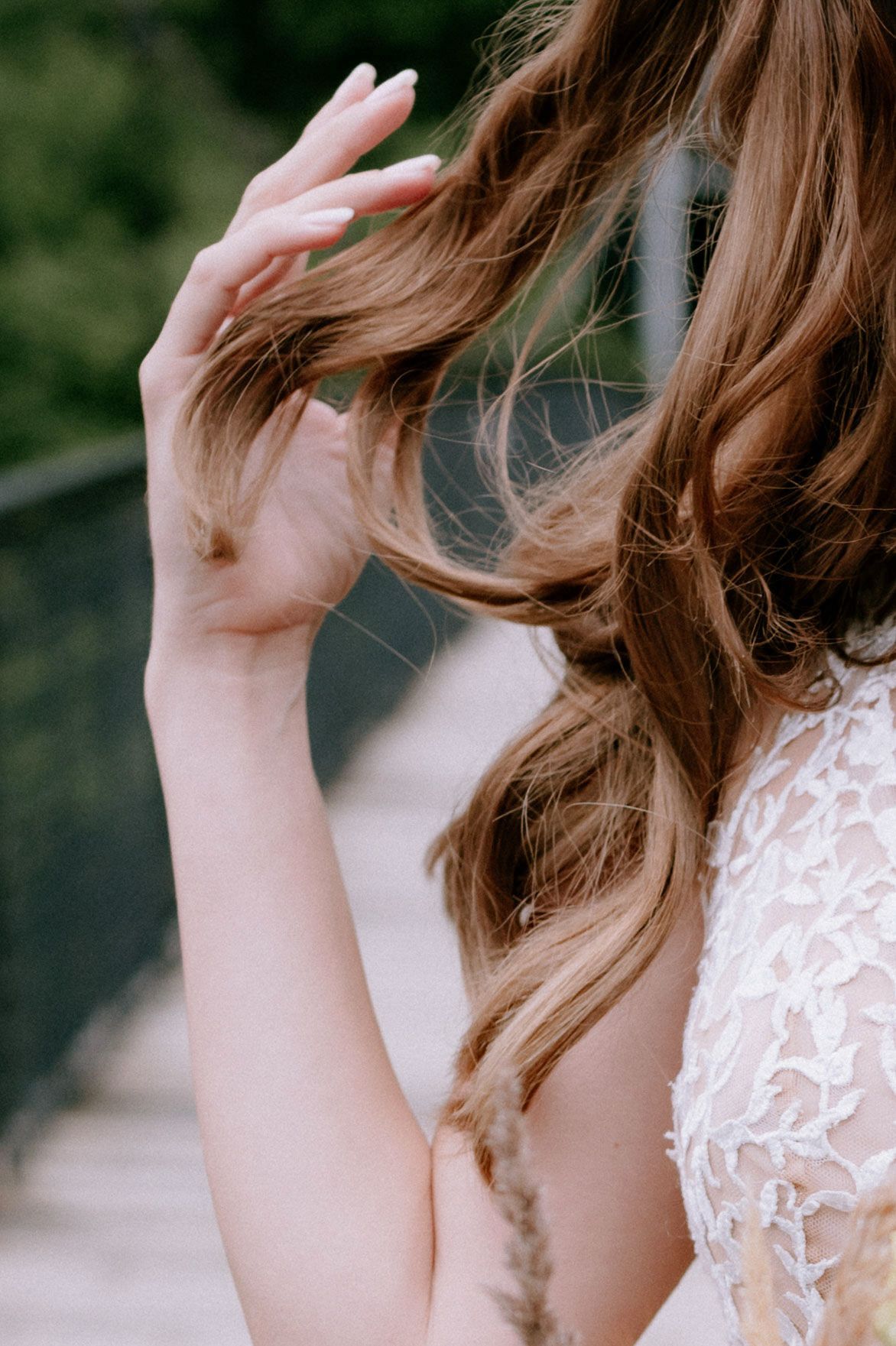 Close-up view of flowing brown hair and delicate white lace detail against a blurred natural background.