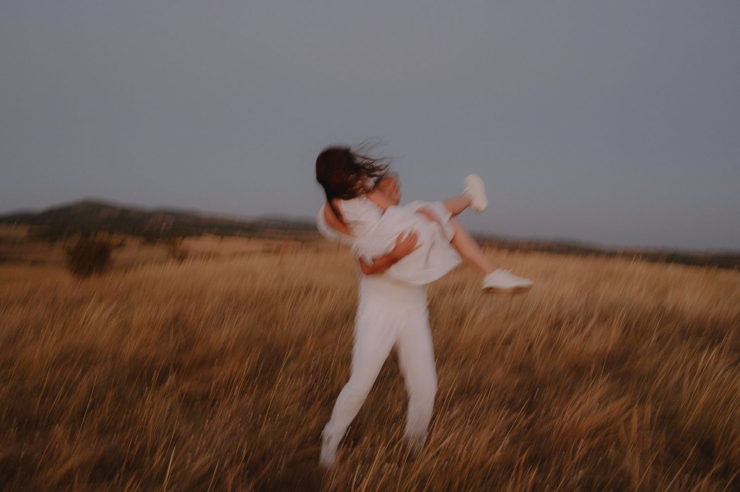 A person in white clothing dances gracefully across a golden field at sunset.