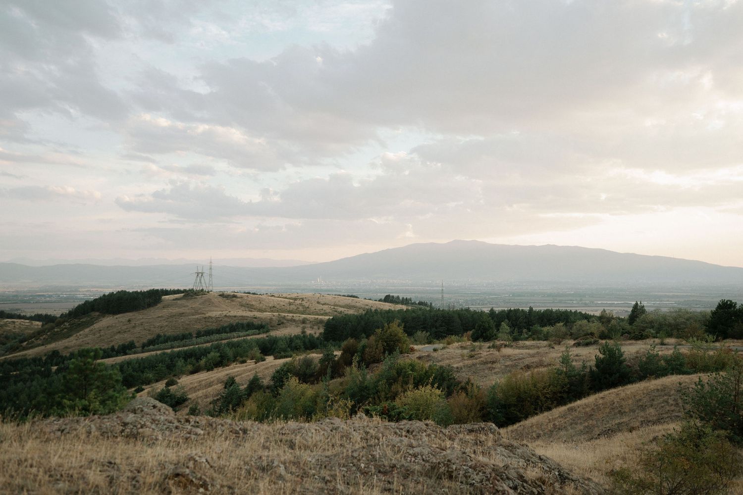 Rolling hills stretch across a panoramic landscape under cloudy skies at sunset.