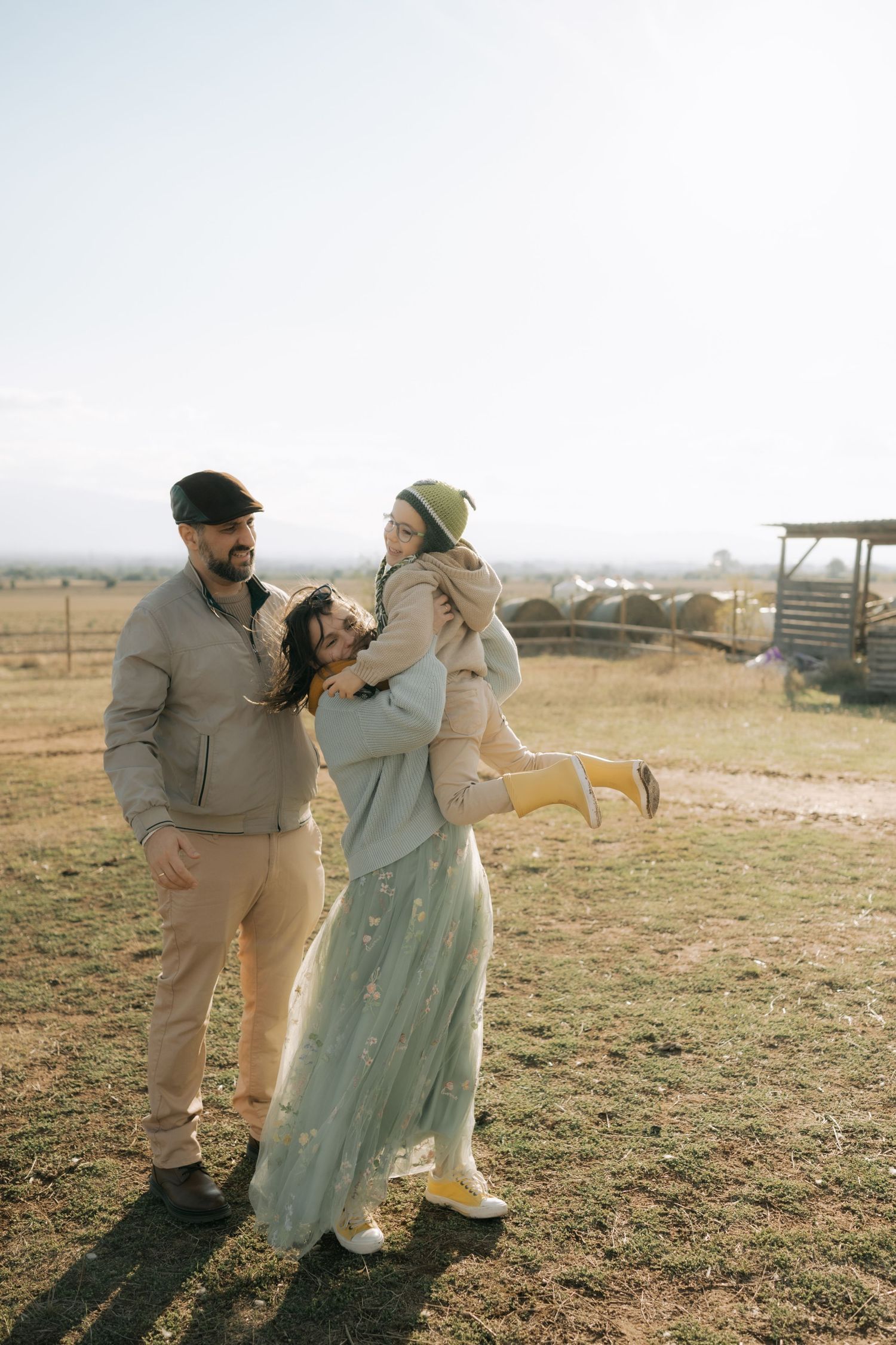 A couple in casual attire playfully dancing together in a golden field at sunset.