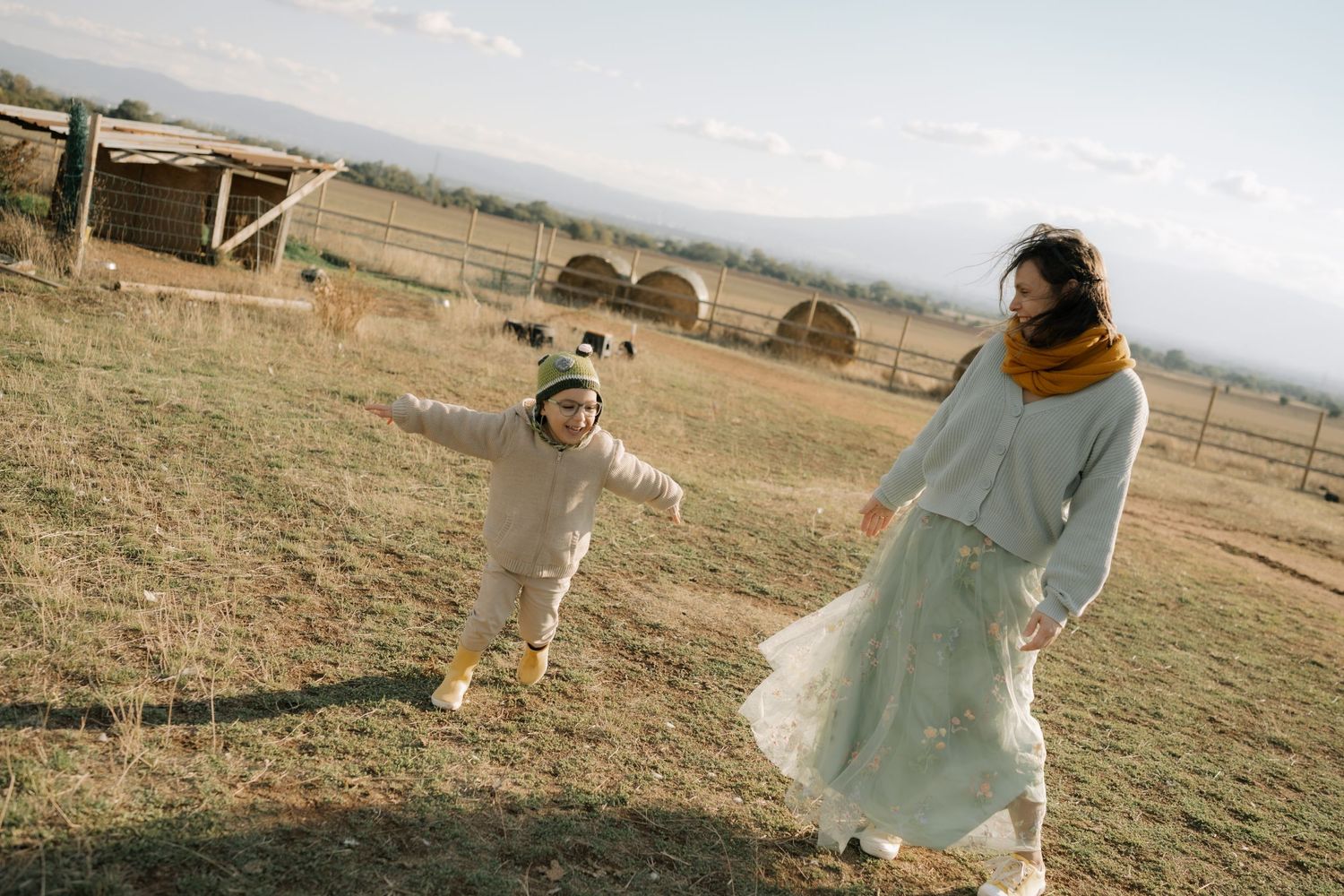 A person in a flowing white dress runs playfully through a golden field at sunset.