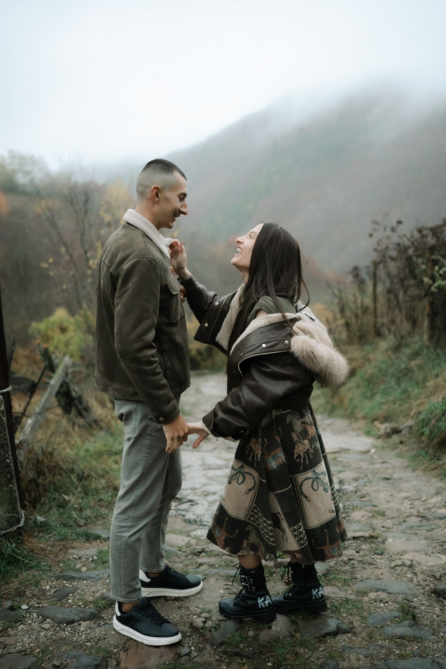 A couple shares an intimate moment on a misty mountain trail during autumn.