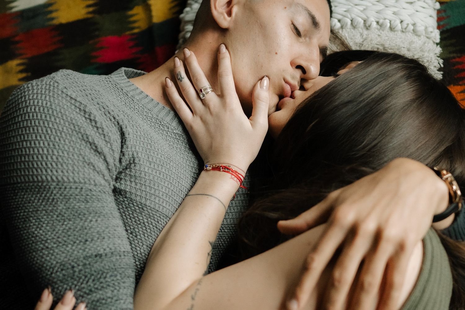Two people share an intimate moment lying close together on a couch in a dimly lit setting.
