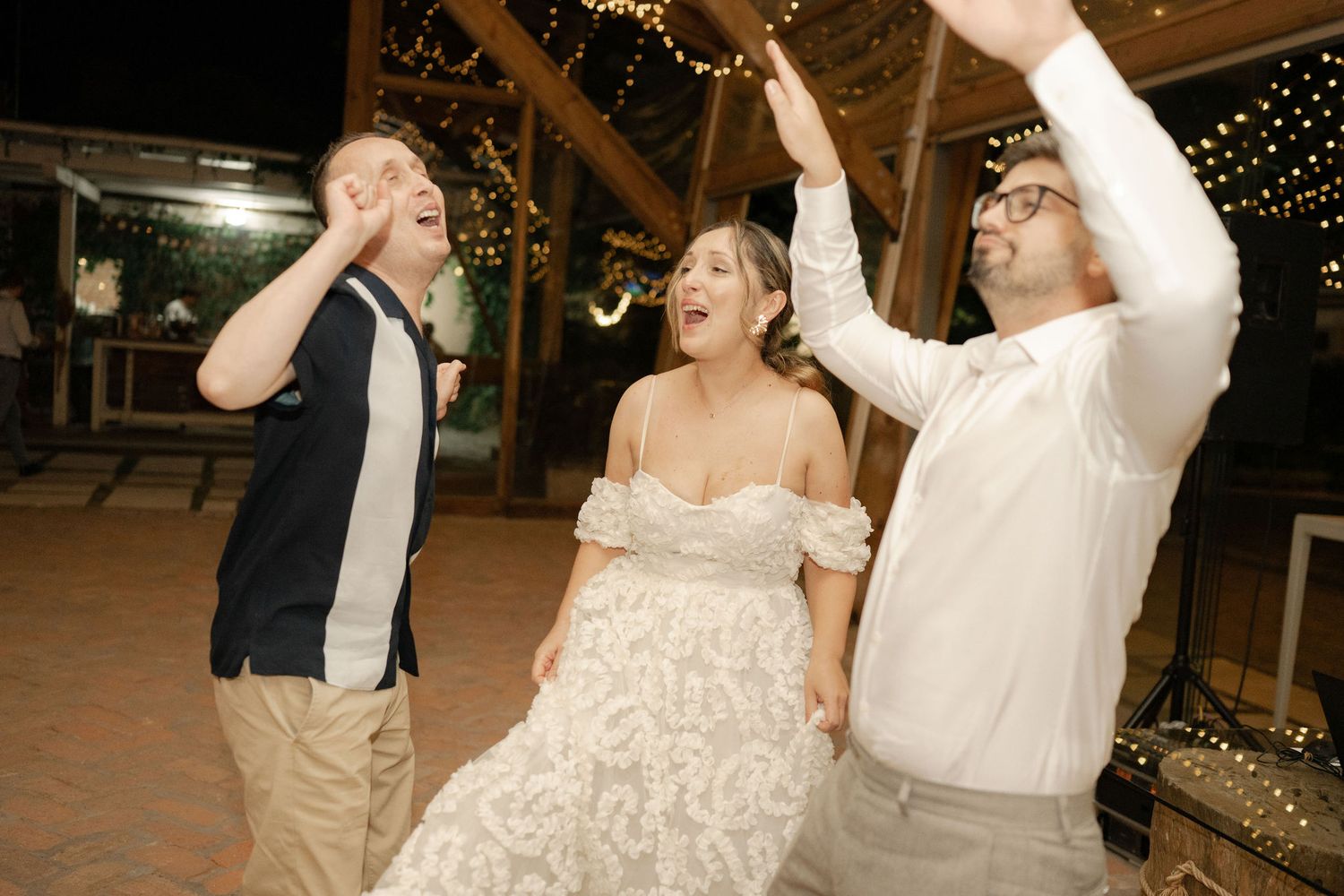 A couple dances together at a rustic wedding reception venue decorated with twinkling lights.