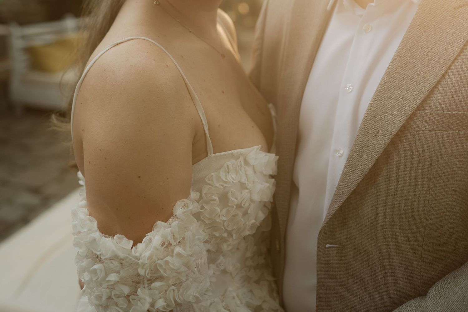 A bride in a white floral wedding dress walks down a rustic wooden staircase with sunlight streaming in.