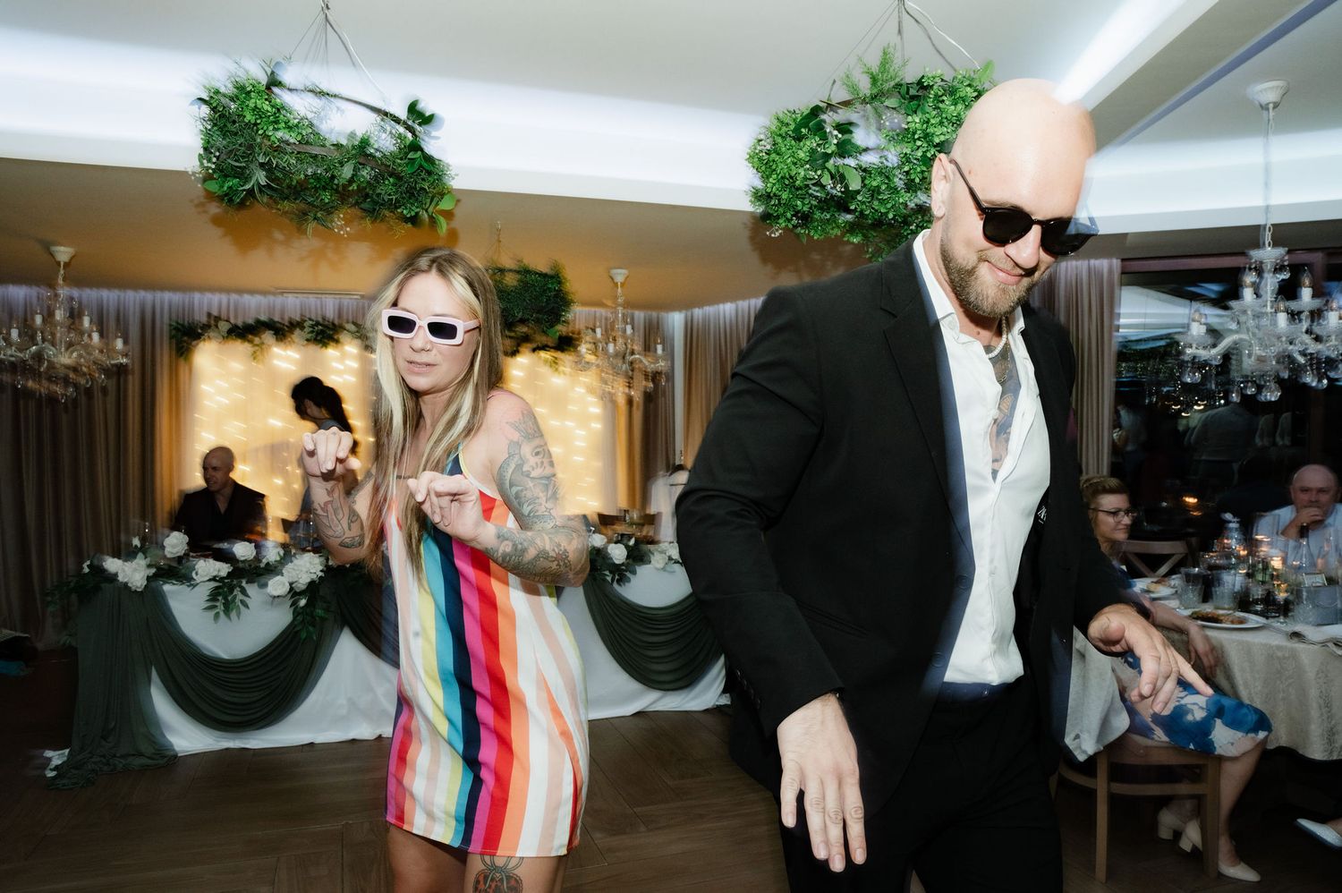 People dancing and celebrating at what appears to be a wedding reception or party venue with indoor lighting.
