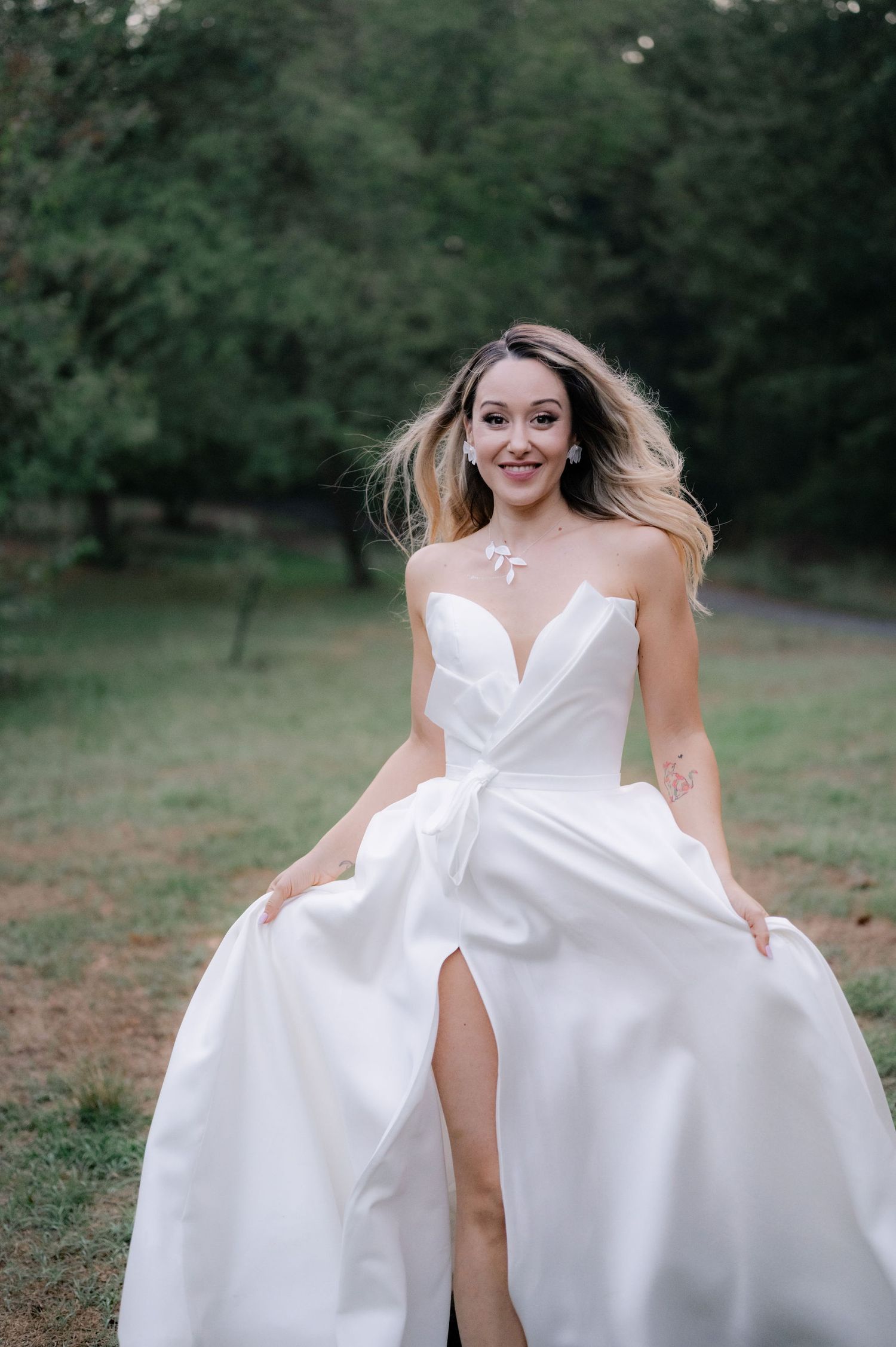 A person in a flowing white wedding dress twirls playfully in a grassy outdoor setting during a photo session.