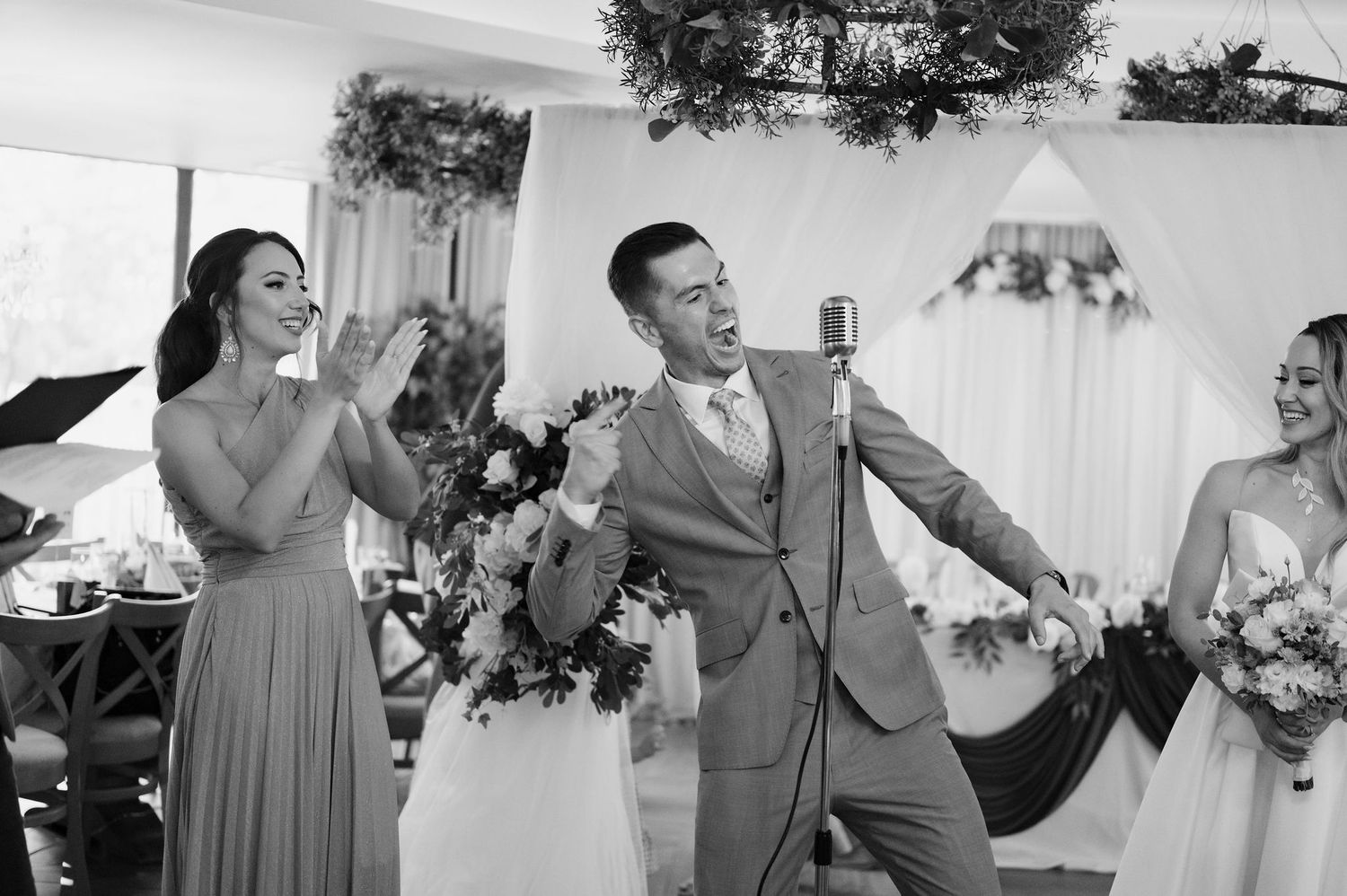 Wedding party members in gray dresses and suits dance joyfully at a reception celebration.