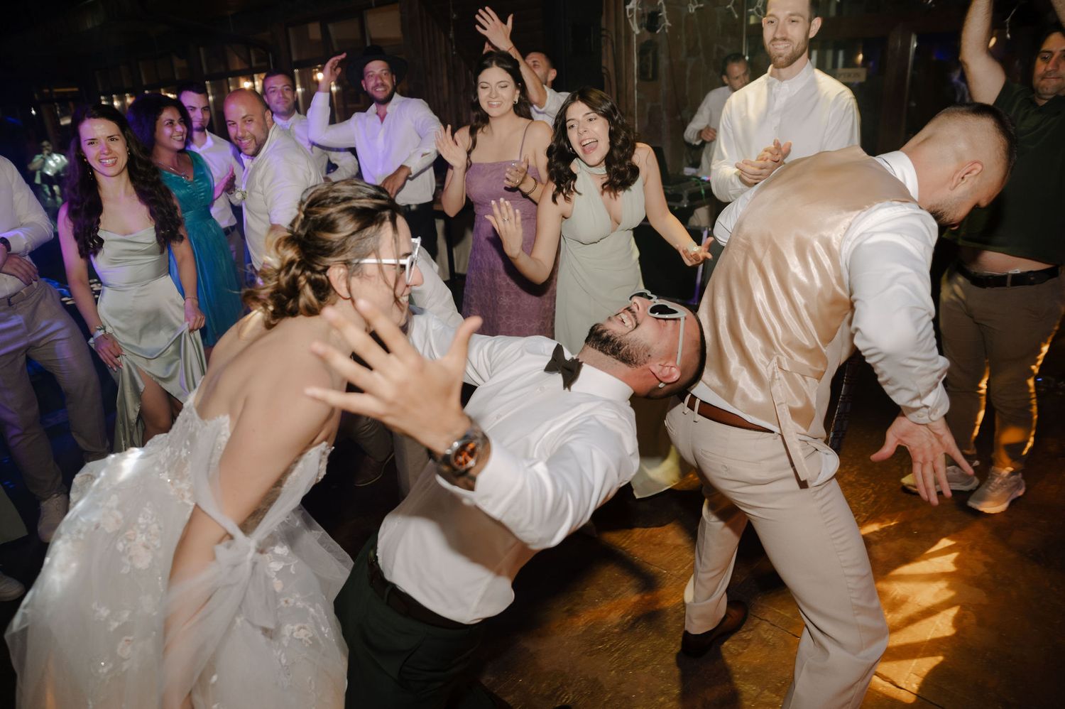 Wedding guests dancing and celebrating on a dimly lit dance floor at a reception party.