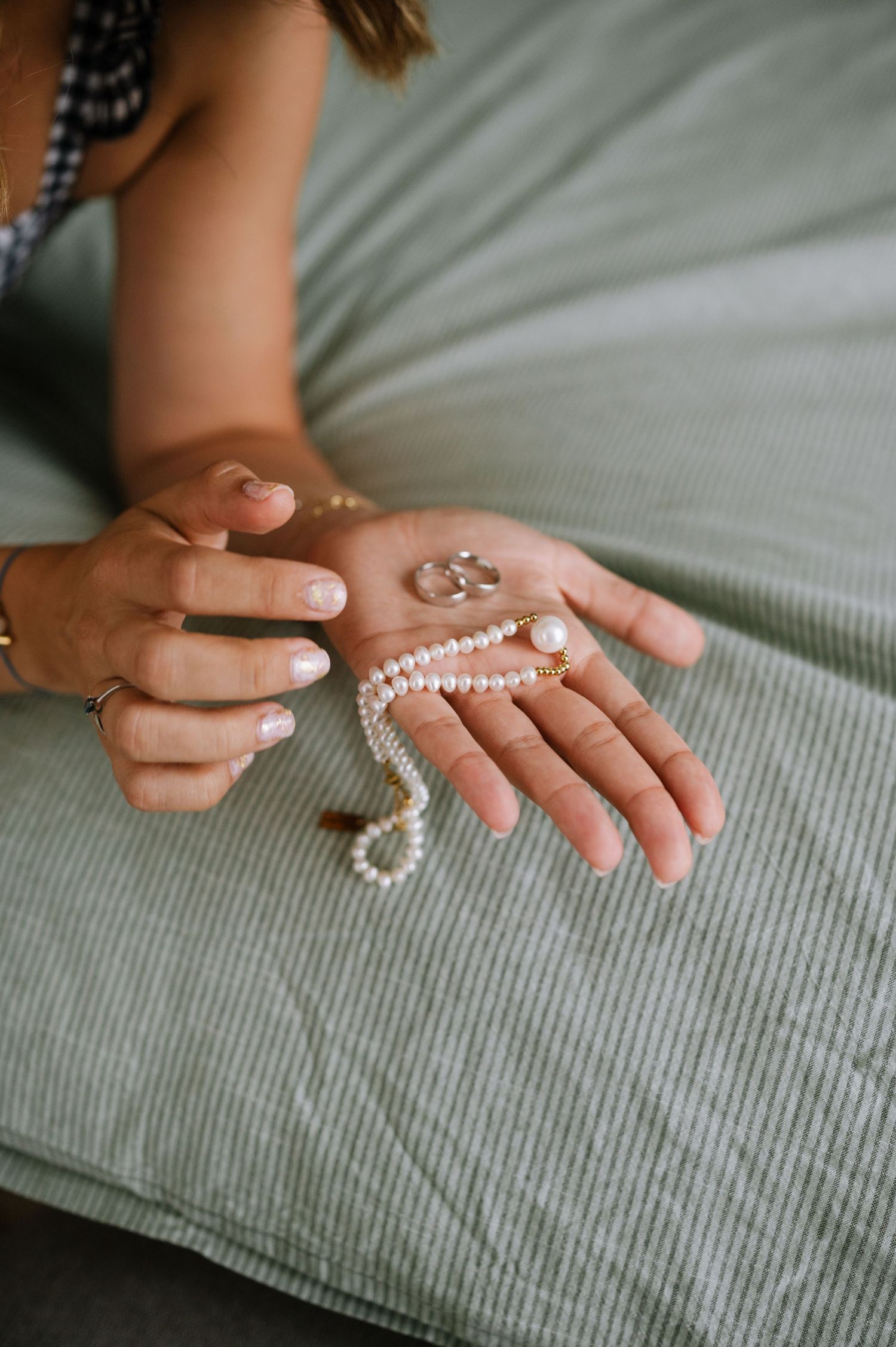 A string of white pearls is gently draped across an outstretched hand on a gray textured fabric background.