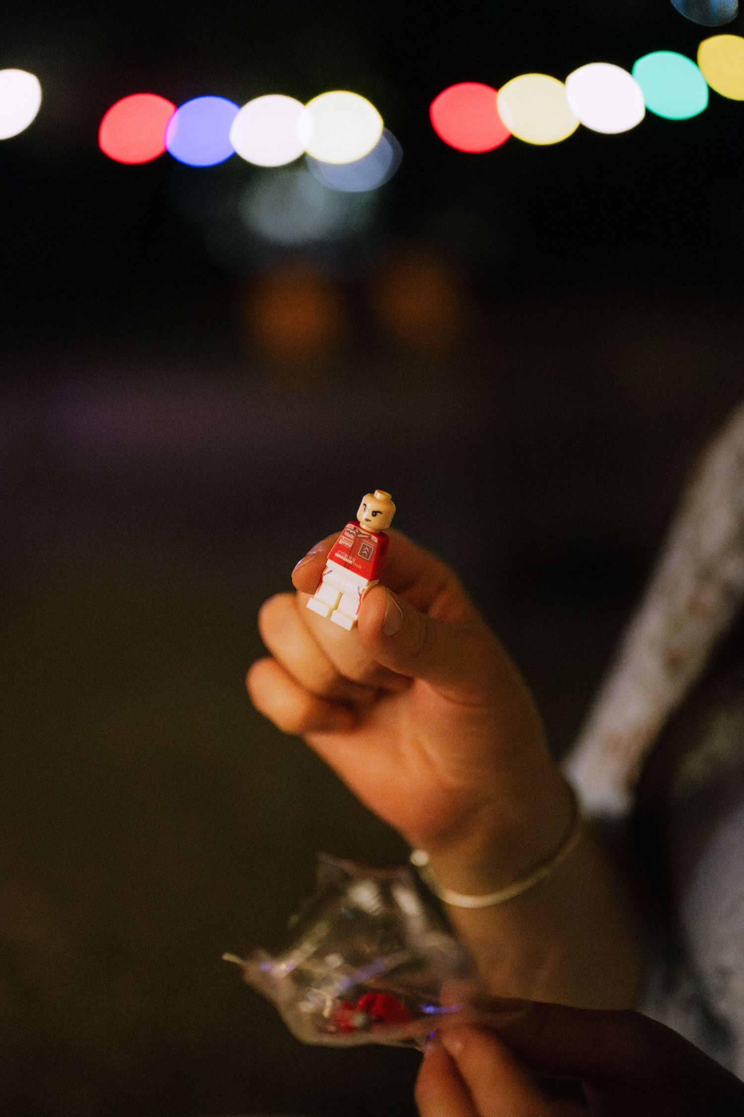 Close-up shot of hands holding small objects with colorful bokeh lights in the dark background.