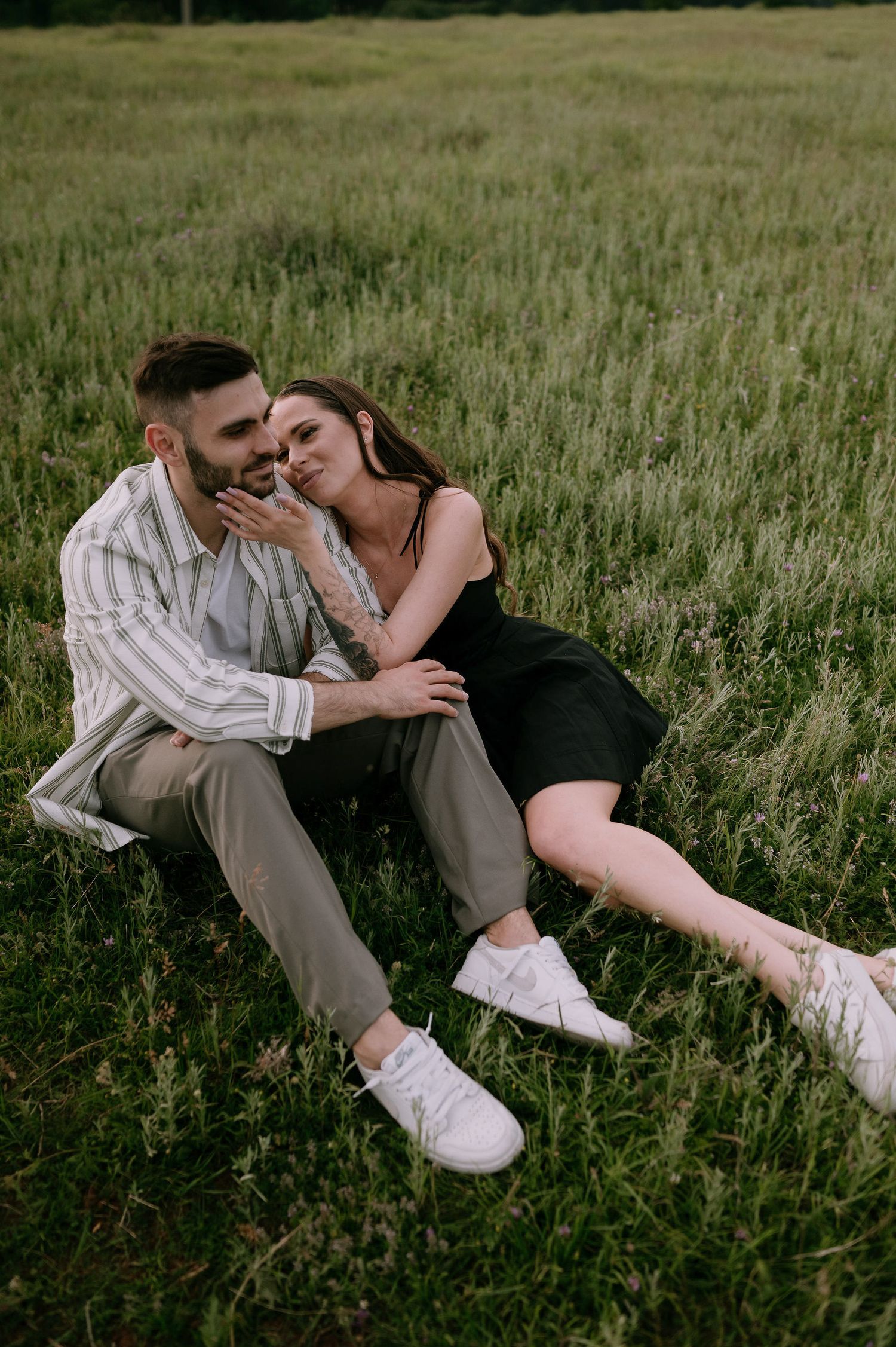 A romantic couple embraces while lying in tall grass during a summer afternoon photoshoot.