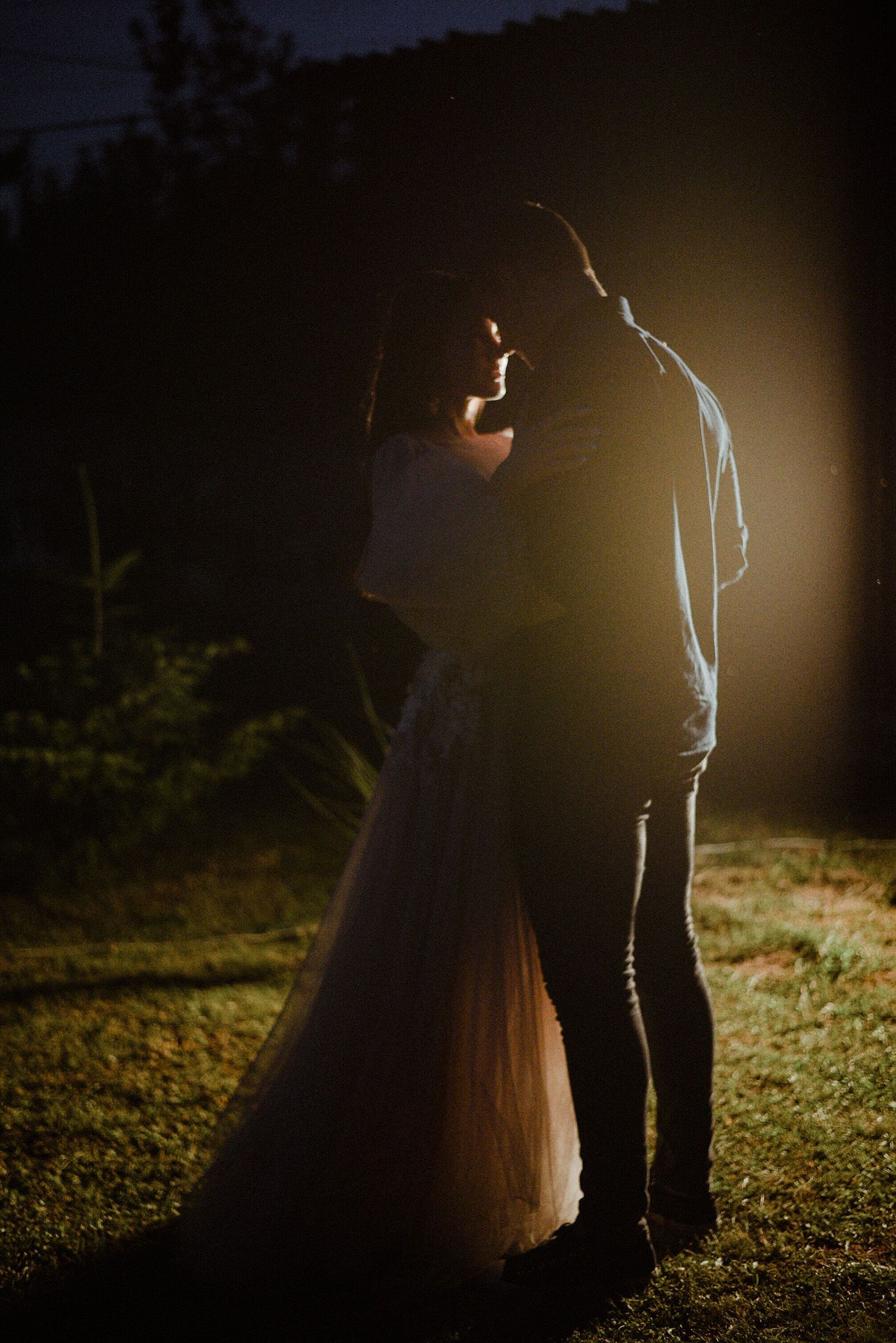 A romantic silhouette of a couple standing close together at night illuminated by dramatic backlighting.