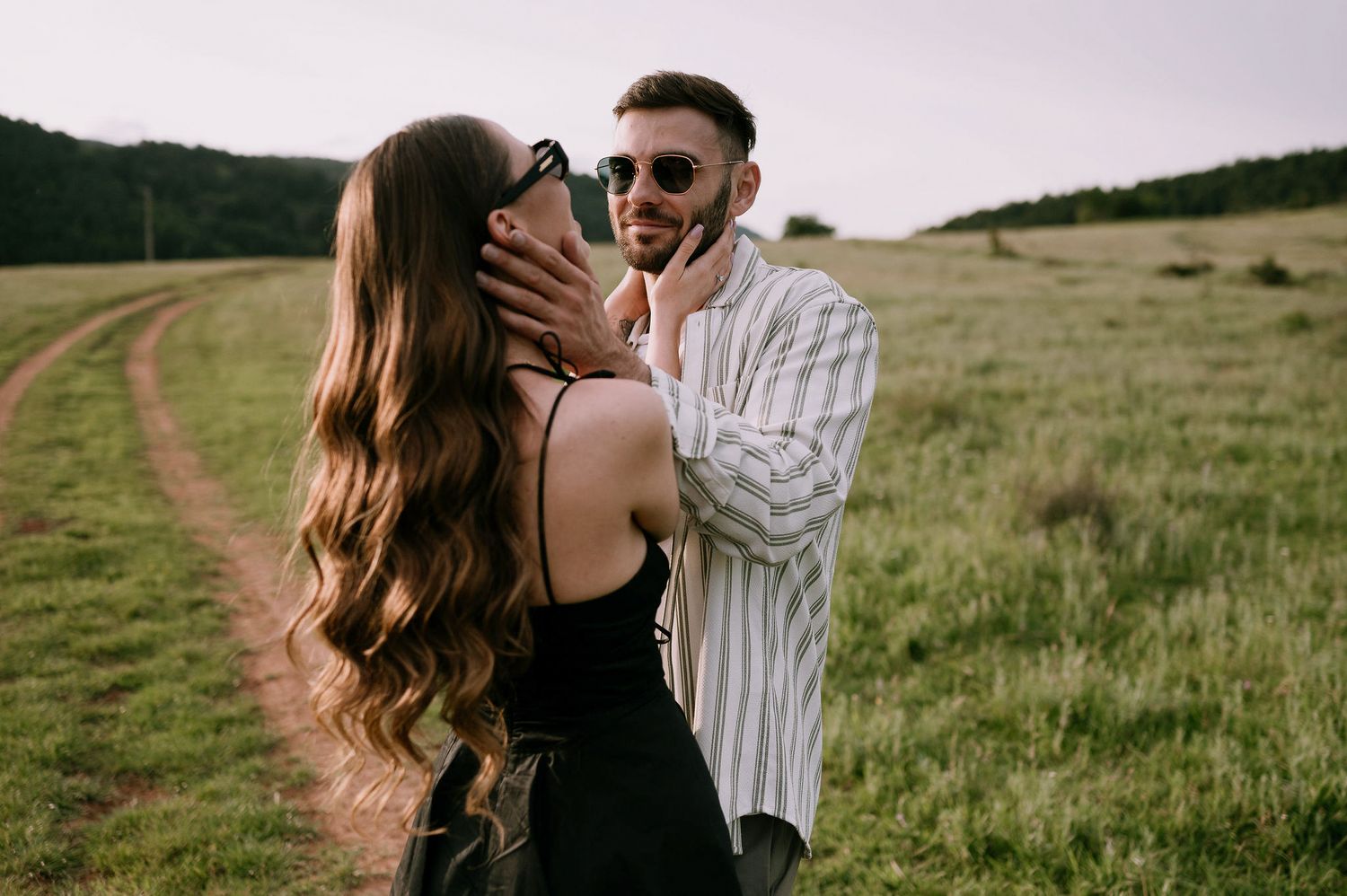 A couple embraces in a romantic moment on a grassy hillside during golden hour.
