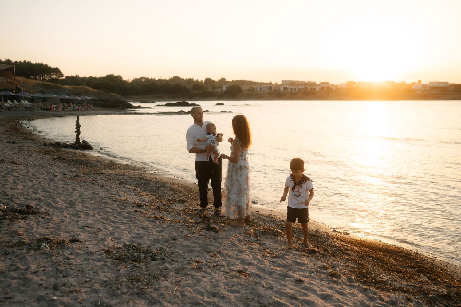 Silhouetted figures walk along a scenic beach shoreline at sunset as golden light reflects off the calm ocean waters.