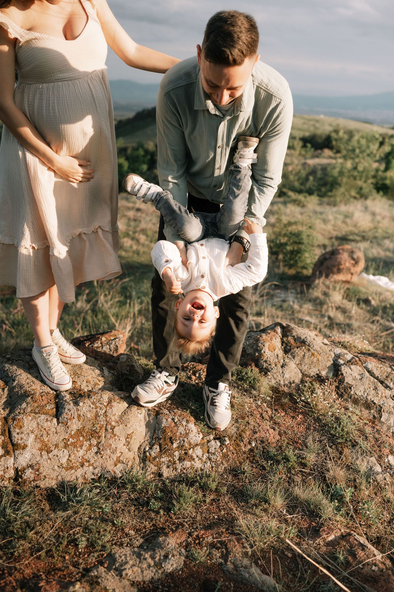 A couple plays with their child on rocky terrain during a sunset photoshoot in nature.