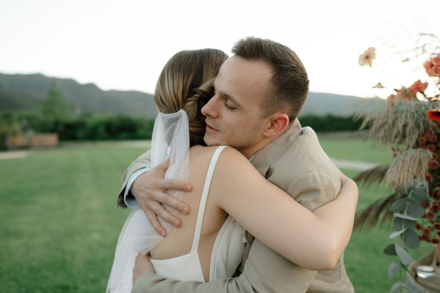 Romantic couple embraces and kisses in a scenic outdoor field during golden hour.
