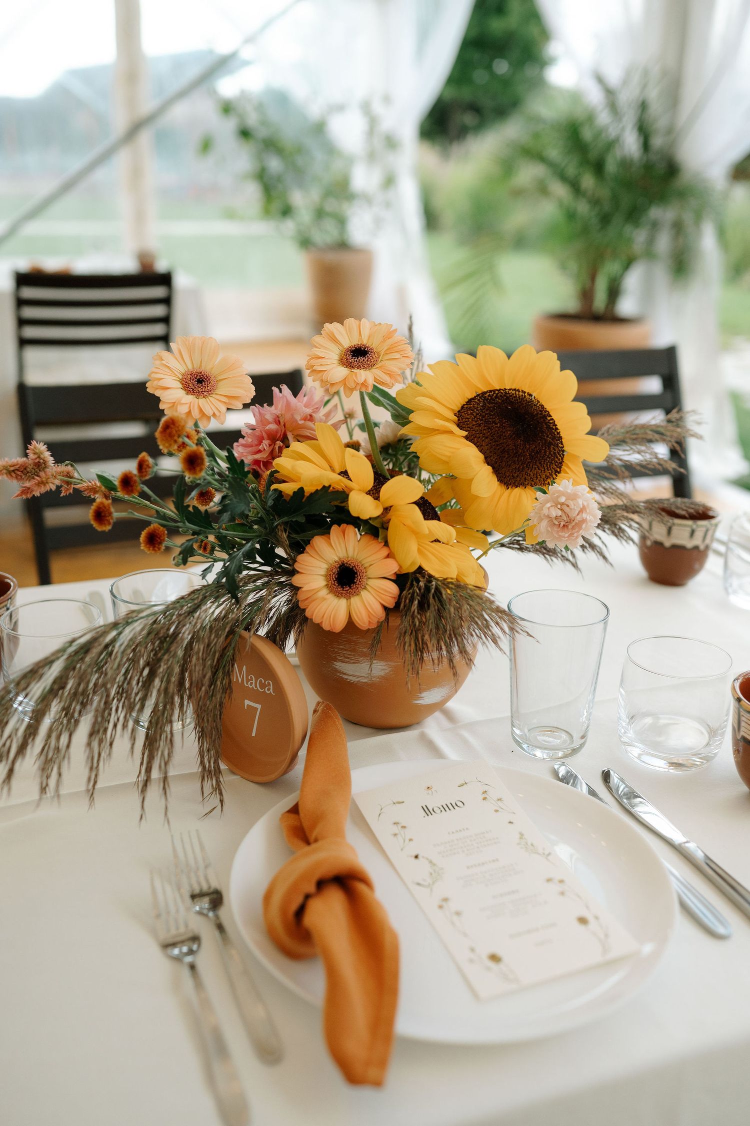 Wedding table setting with sunflowers and orange napkins in a bright conservatory with natural lighting.