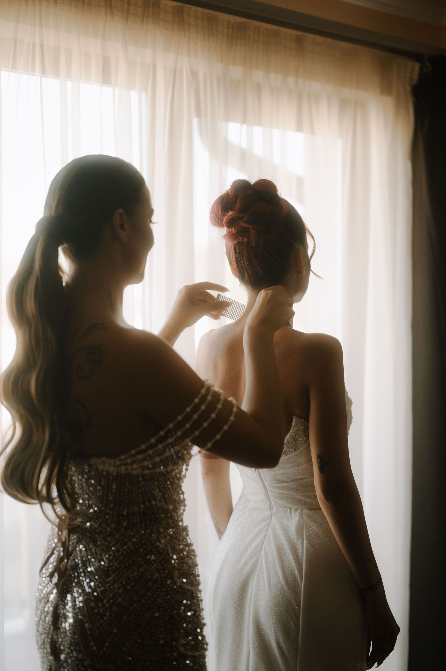 Three silhouettes of women in formal dresses stand against a backlit window creating a dreamy atmosphere.