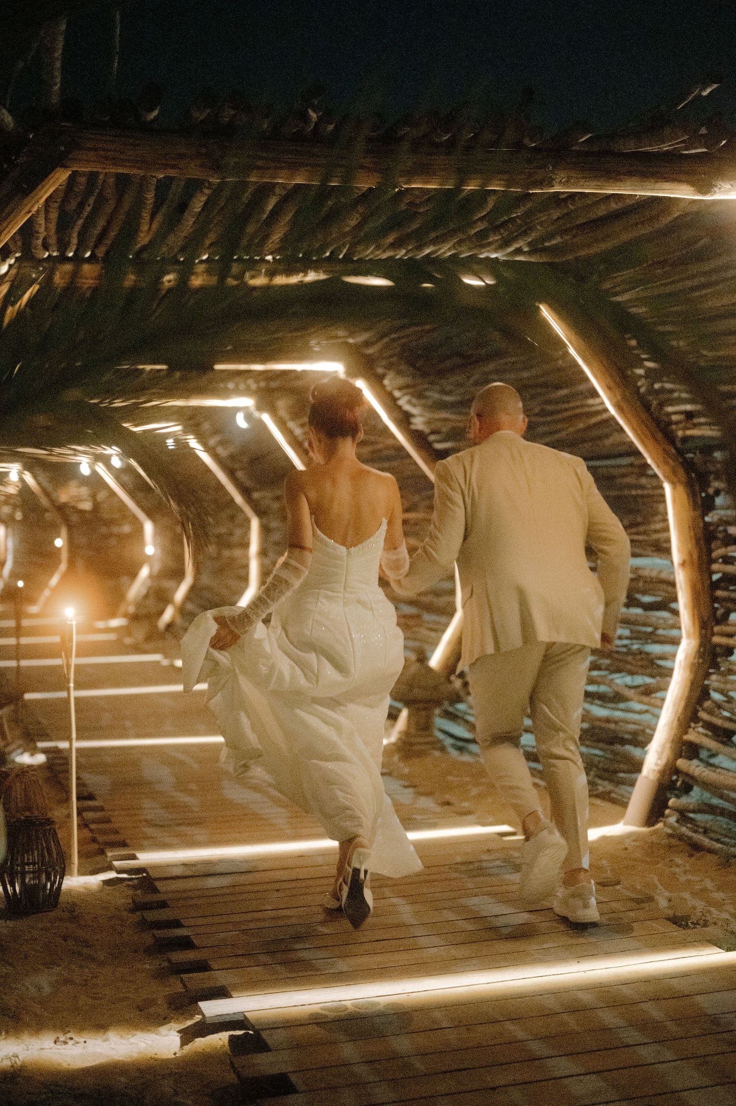 People walking through a dimly lit wooden tunnel with illuminated strips of light creating a dramatic pathway.
