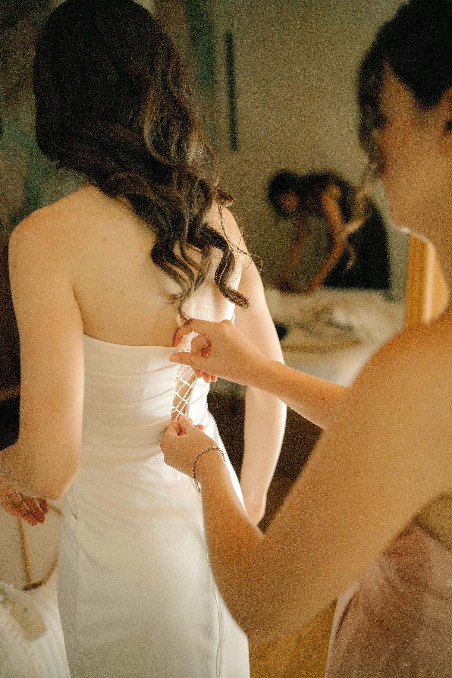 Someone helps lace up a white wedding dress on a bride getting ready before the ceremony.