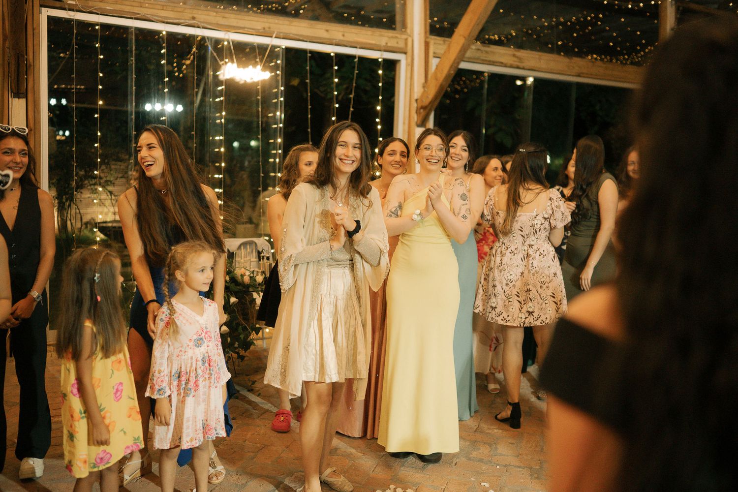 Wedding guests gather on a rustic dance floor with string lights overhead during an evening celebration.