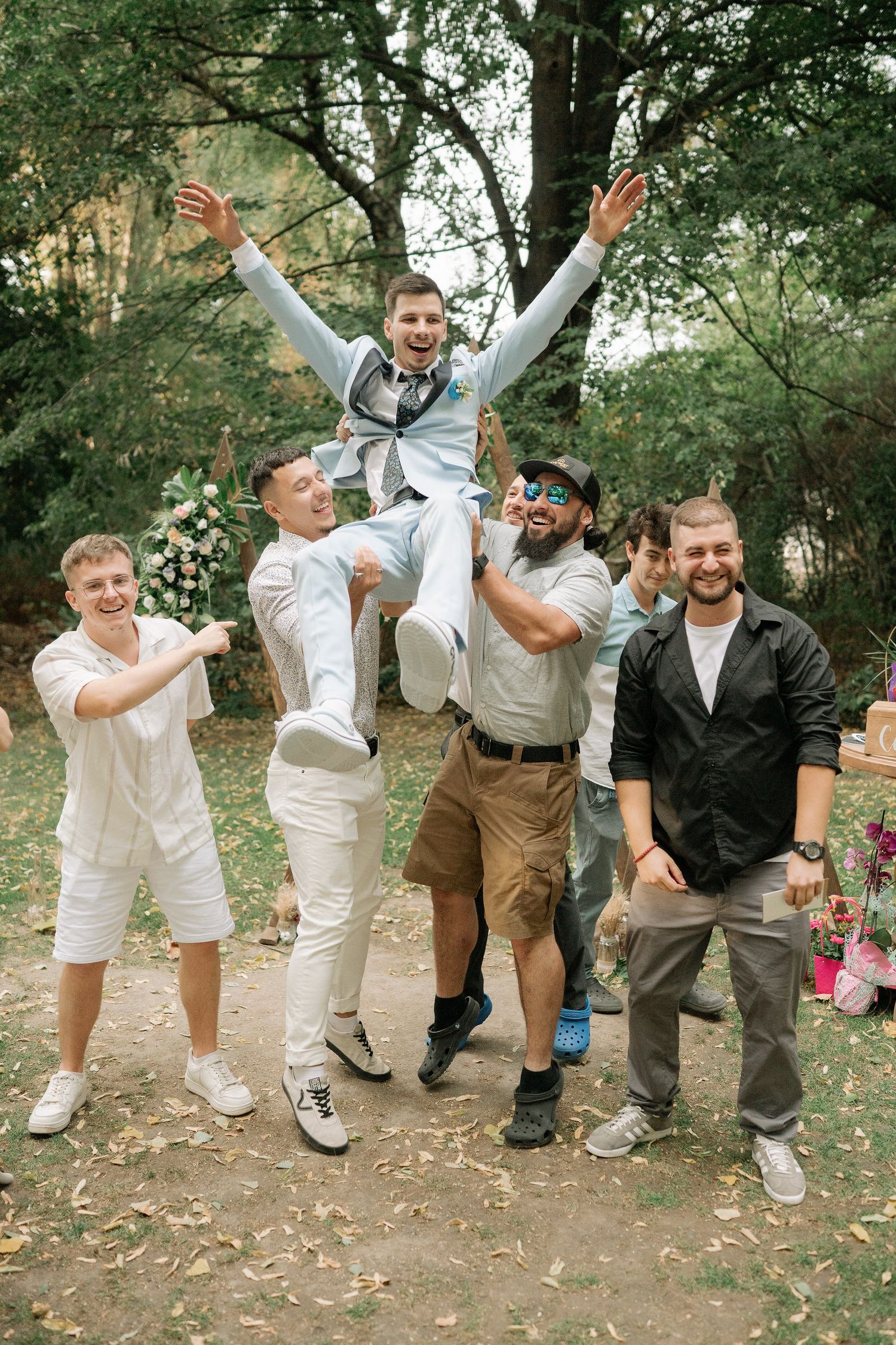 A fun sequence of groomsmen jumping and posing together in casual wedding attire with khaki pants and white shirts outdoors.