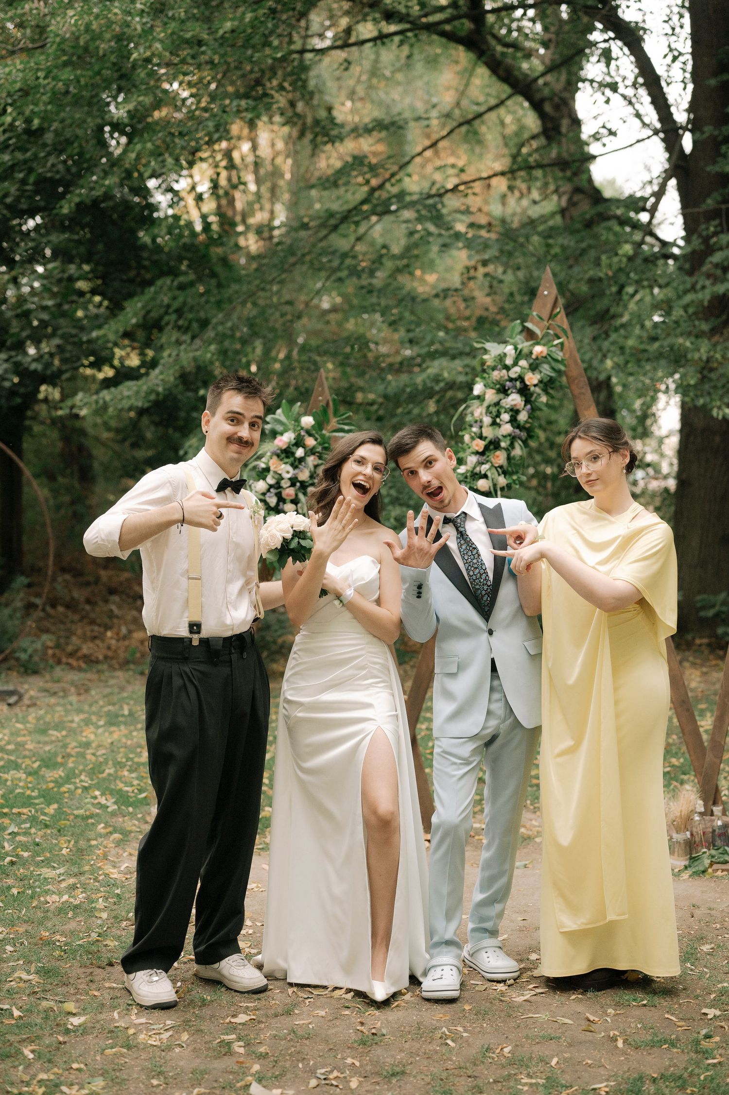 Wedding party in pastel outfits strikes playful poses in a garden setting.