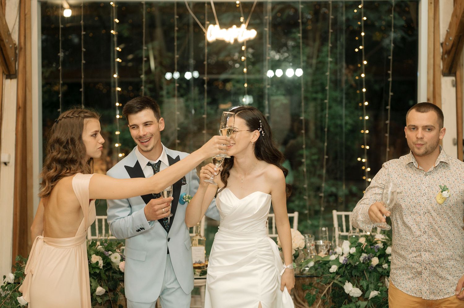 Wedding party celebrates at an elegant reception venue with glass walls and decorative greenery.